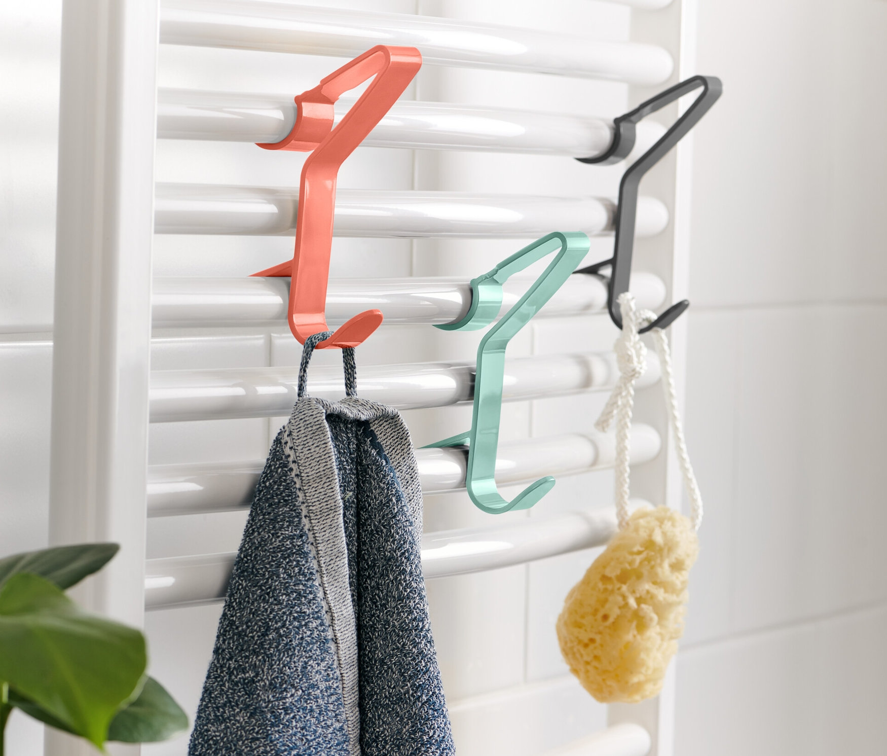 Na białym grzejniku wiszą 3 haczyki na grzejnik, na których wiszą ręcznik i gąbka.