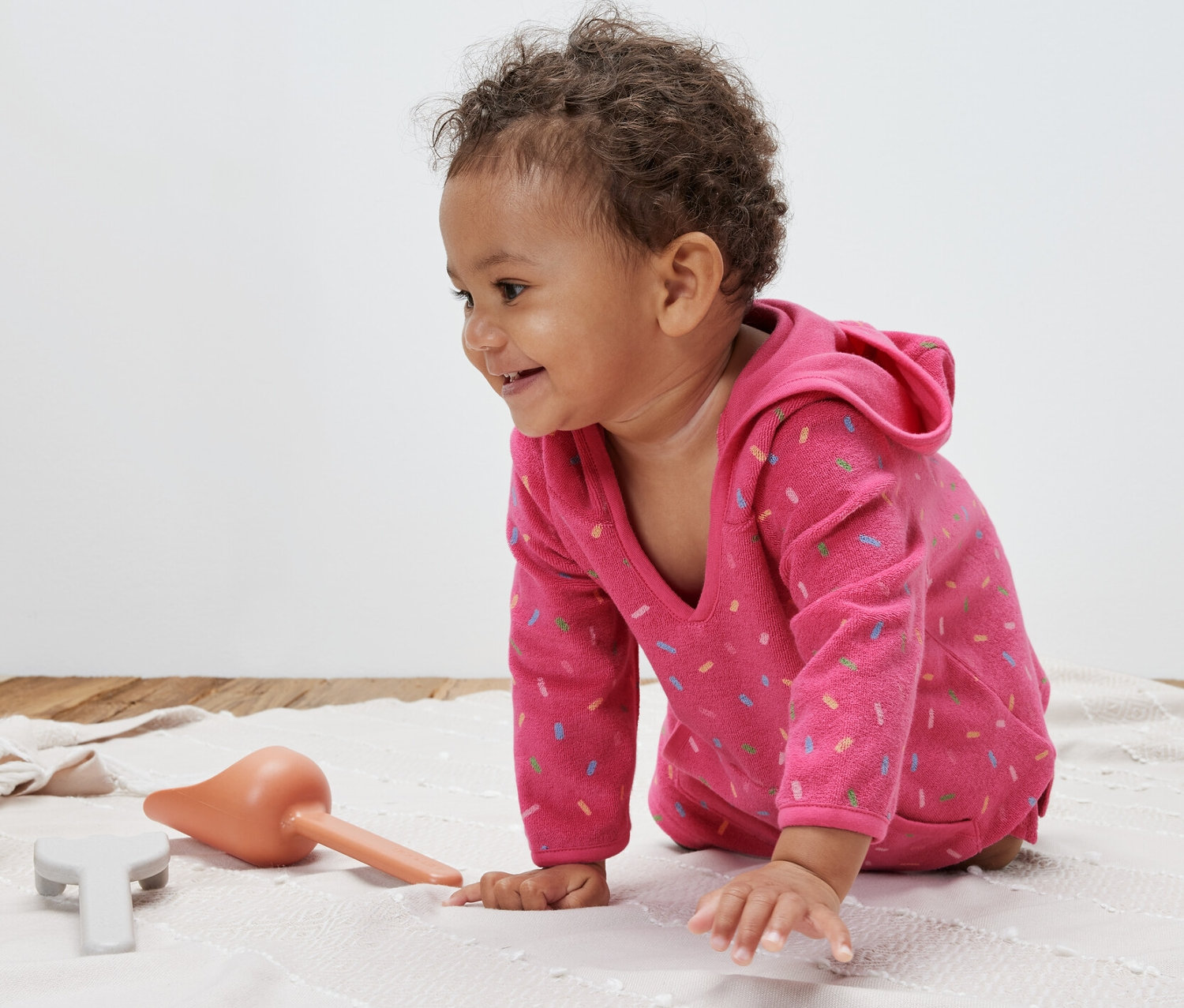 Niemowlę raczkuje na kocu, ubrane w różowe ponczo frotte.