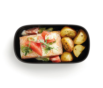 W czarnym pojemniku na lunch znajduje się łosoś z ziemniakami.