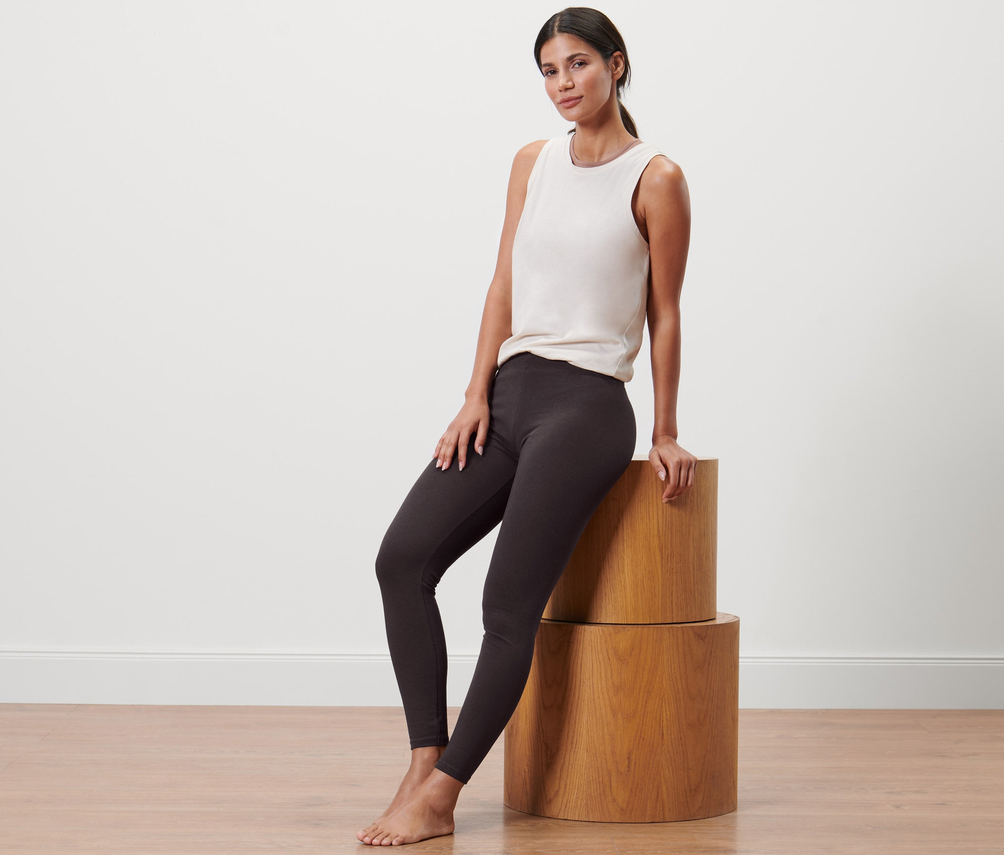 Kobieta siedzi na drewnianych cylindrach, ma na sobie legginsy sportowe i podkoszulek.
