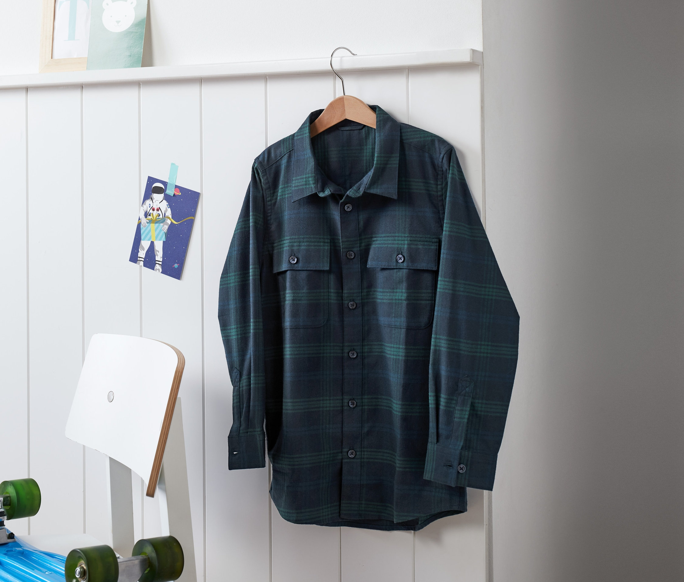Na wieszaku wisi granatowo-zielona koszula flanelowa w kratę.