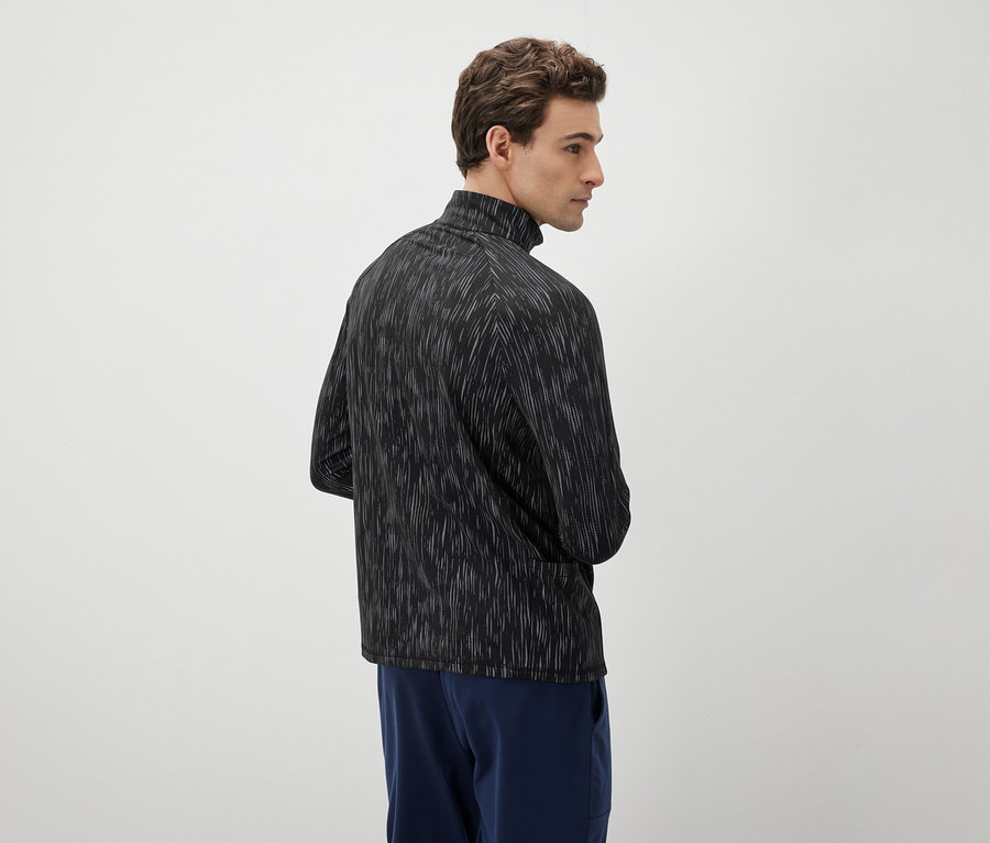 Mężczyzna patrzy w lewo, ma na sobie czarno-białą bluzkę i niebieskie spodnie.