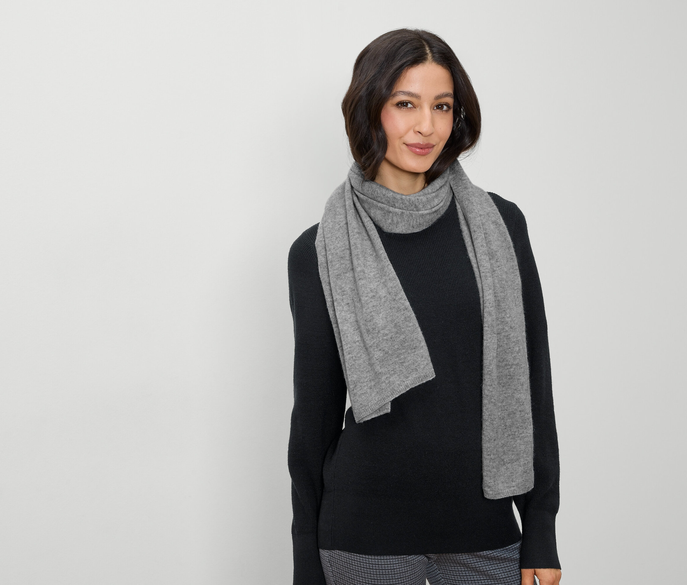 Kobieta z brązowymi włosami i szarym szalikiem pozuje na jasnym tle.