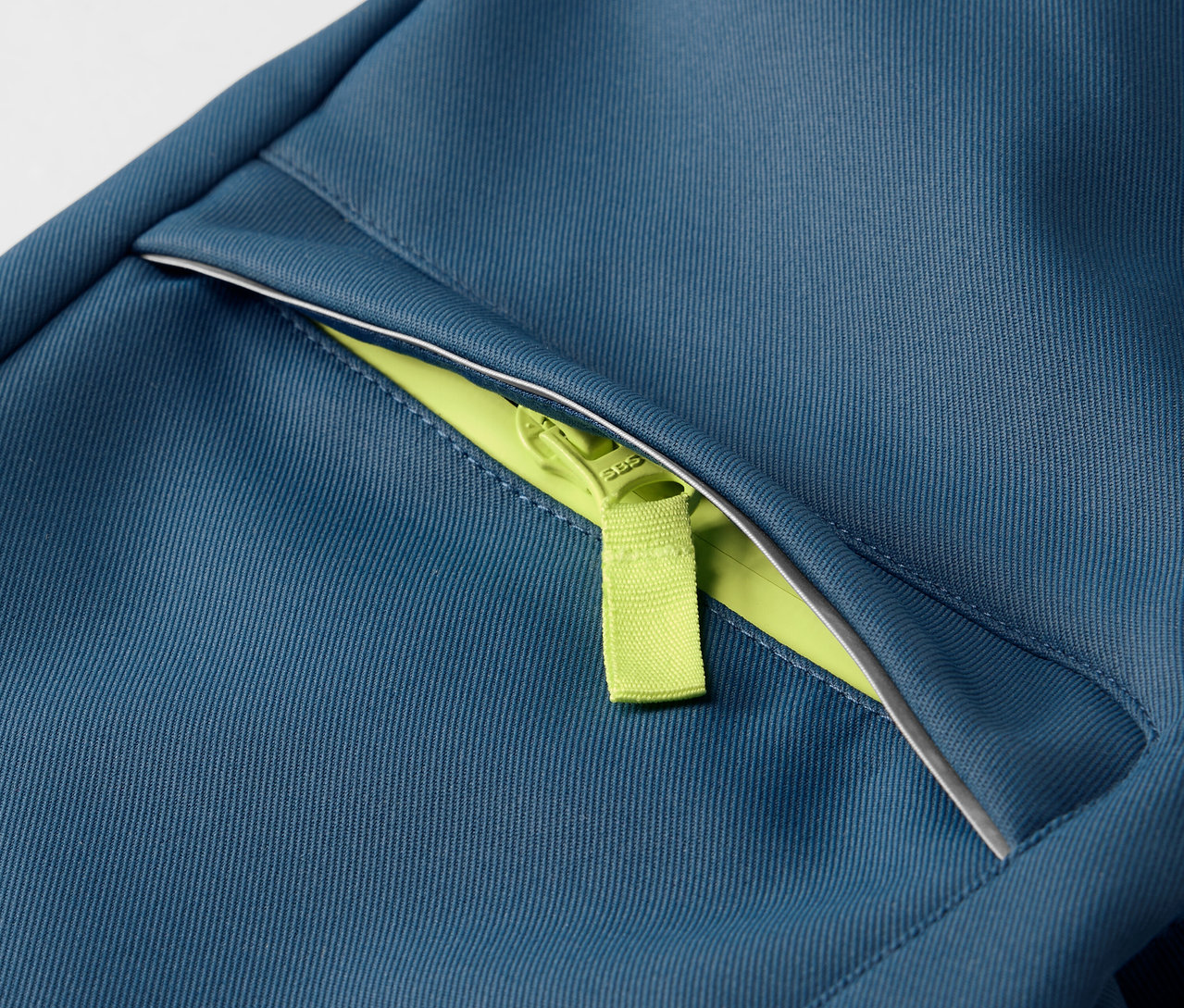 Zbliżenie na spodnie softshell dla dzieci z neonowo zielonym zamkiem błyskawicznym.