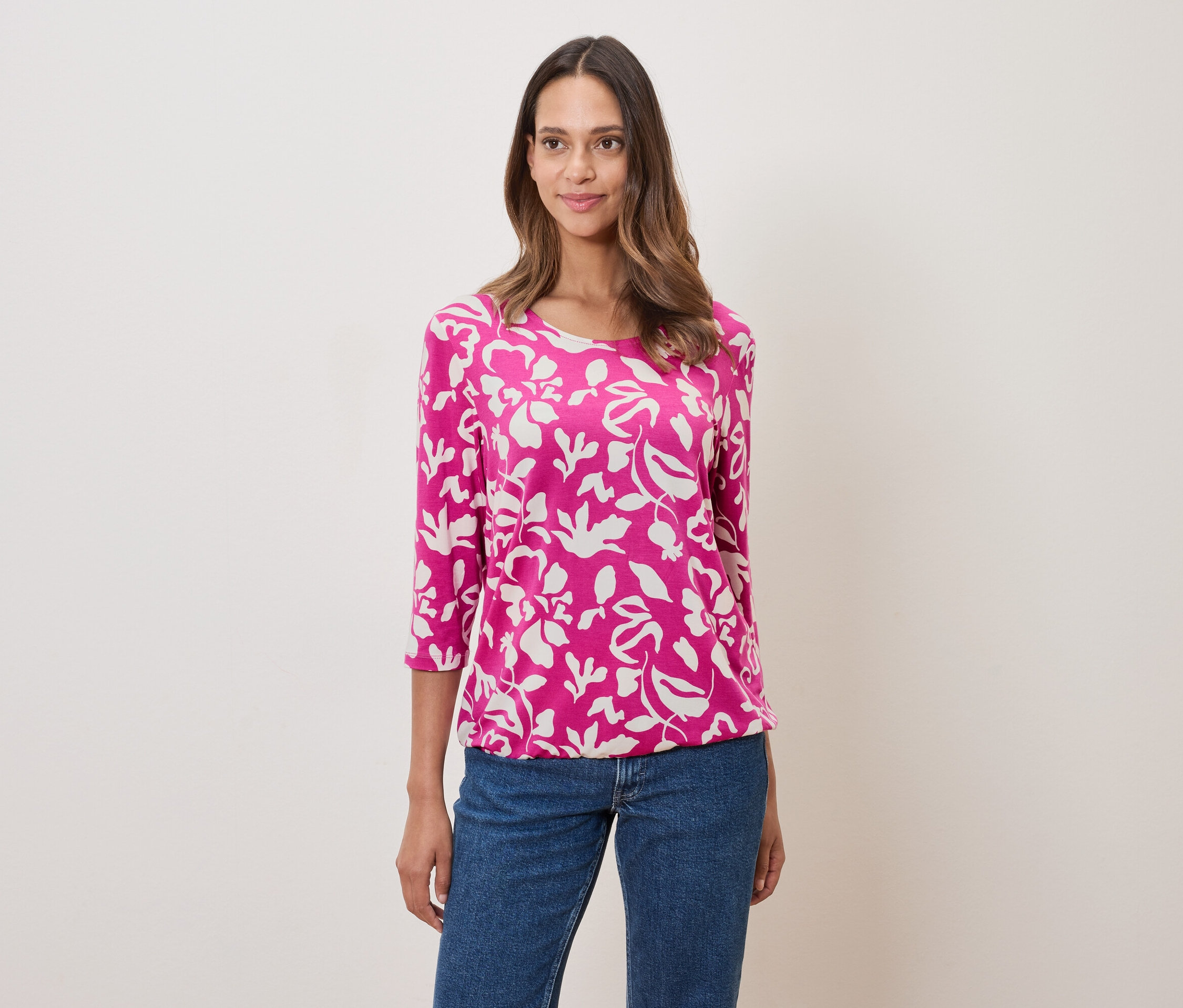 Kobieta ma na sobie różową bluzkę w kwiaty i dżinsy.