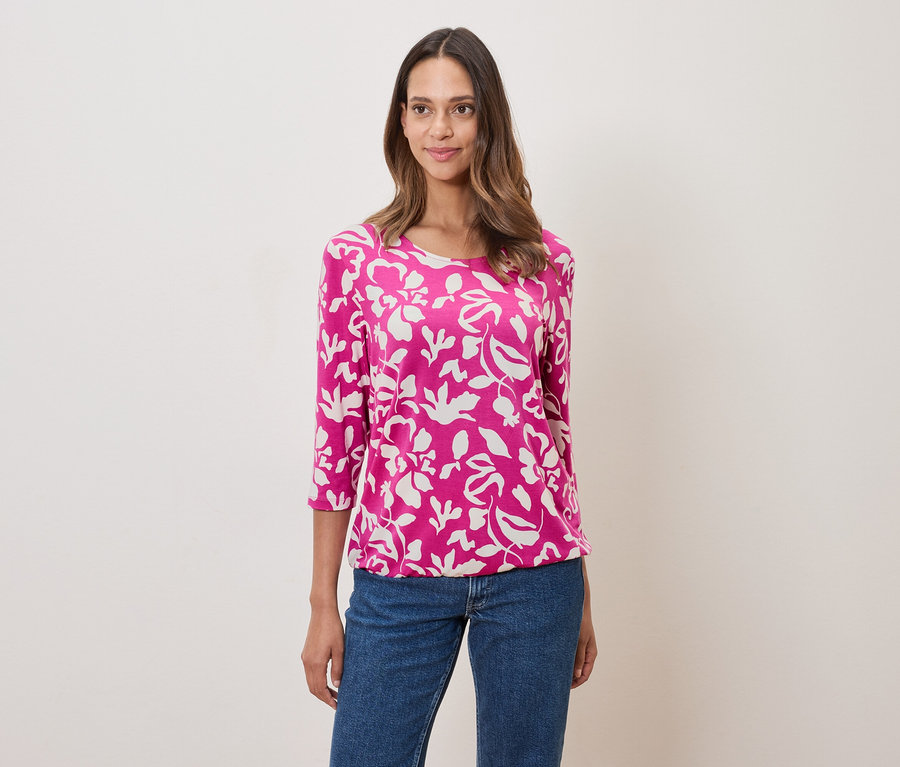 Kobieta ma na sobie różową bluzkę w kwiaty i dżinsy.