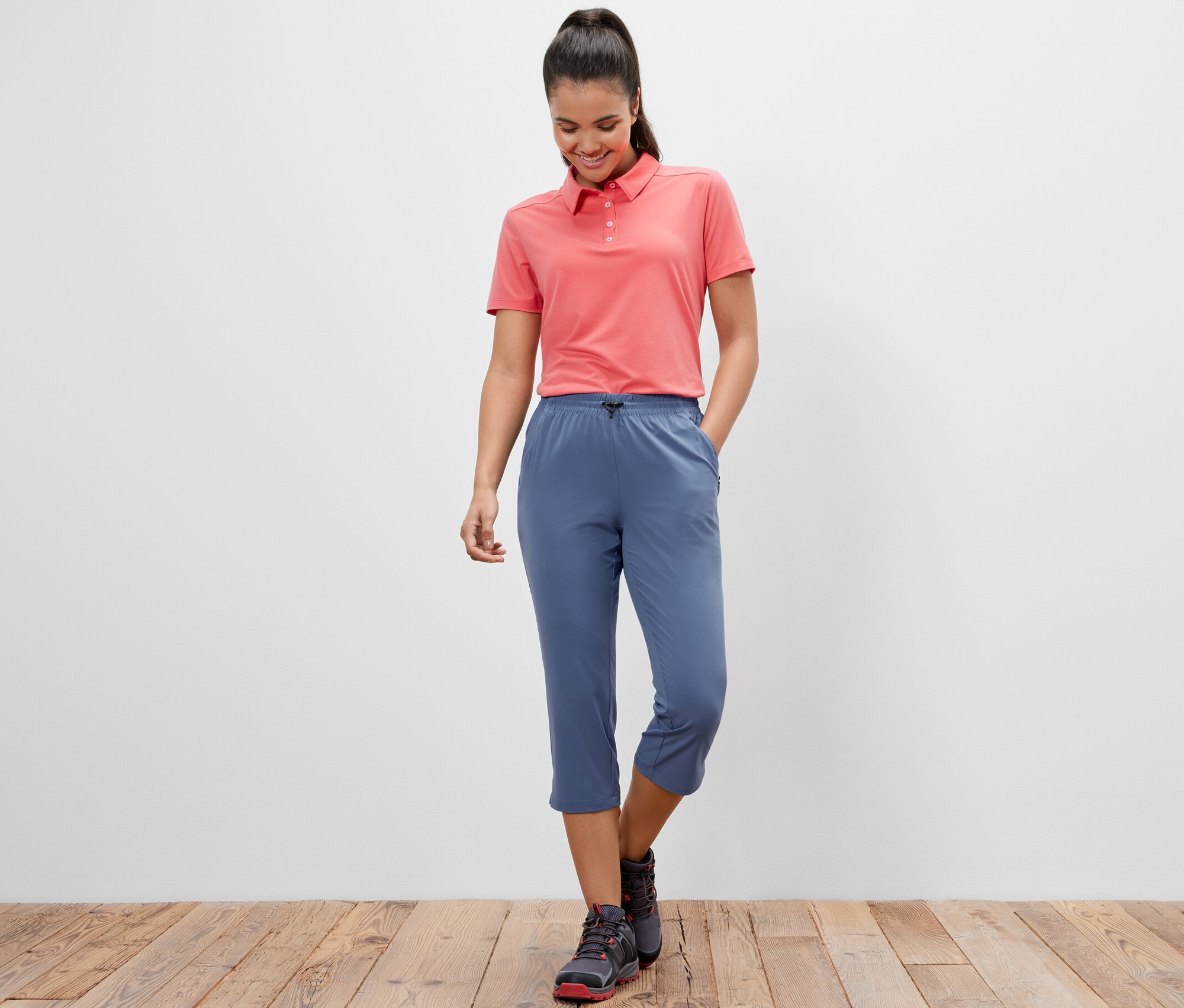 Kobieta ma na sobie różową koszulkę polo i niebieskie funkcyjne spodnie capri.