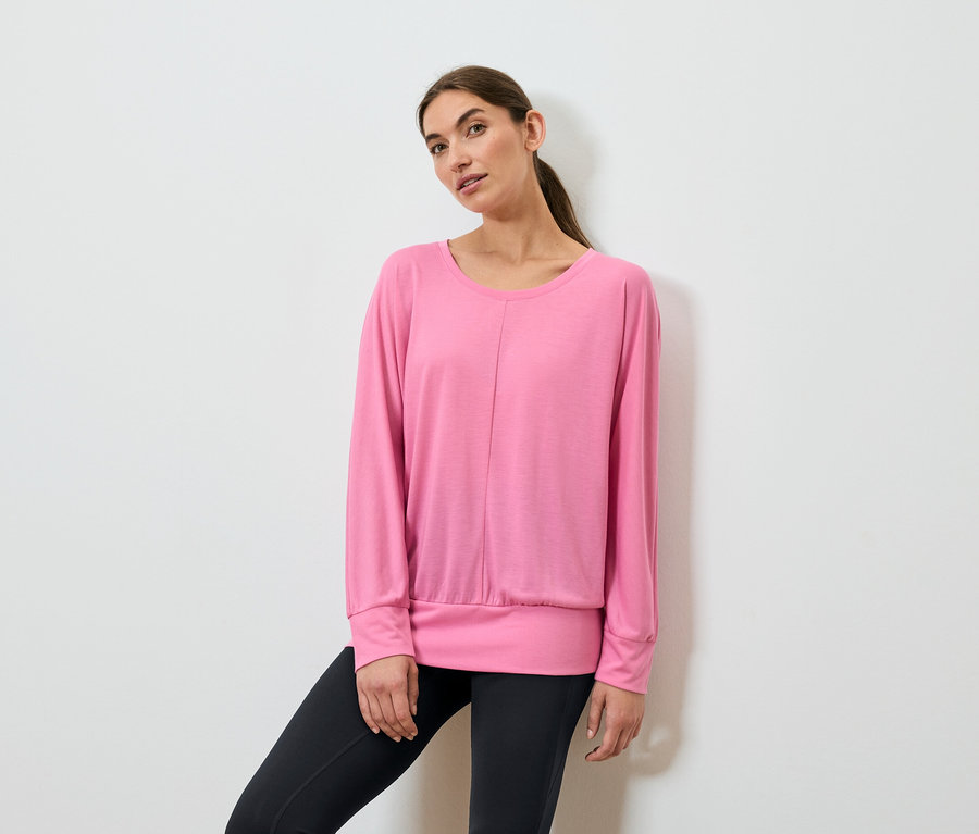 Kobieta pozuje w różowym sportowym topie z długim rękawem i czarnych legginsach.