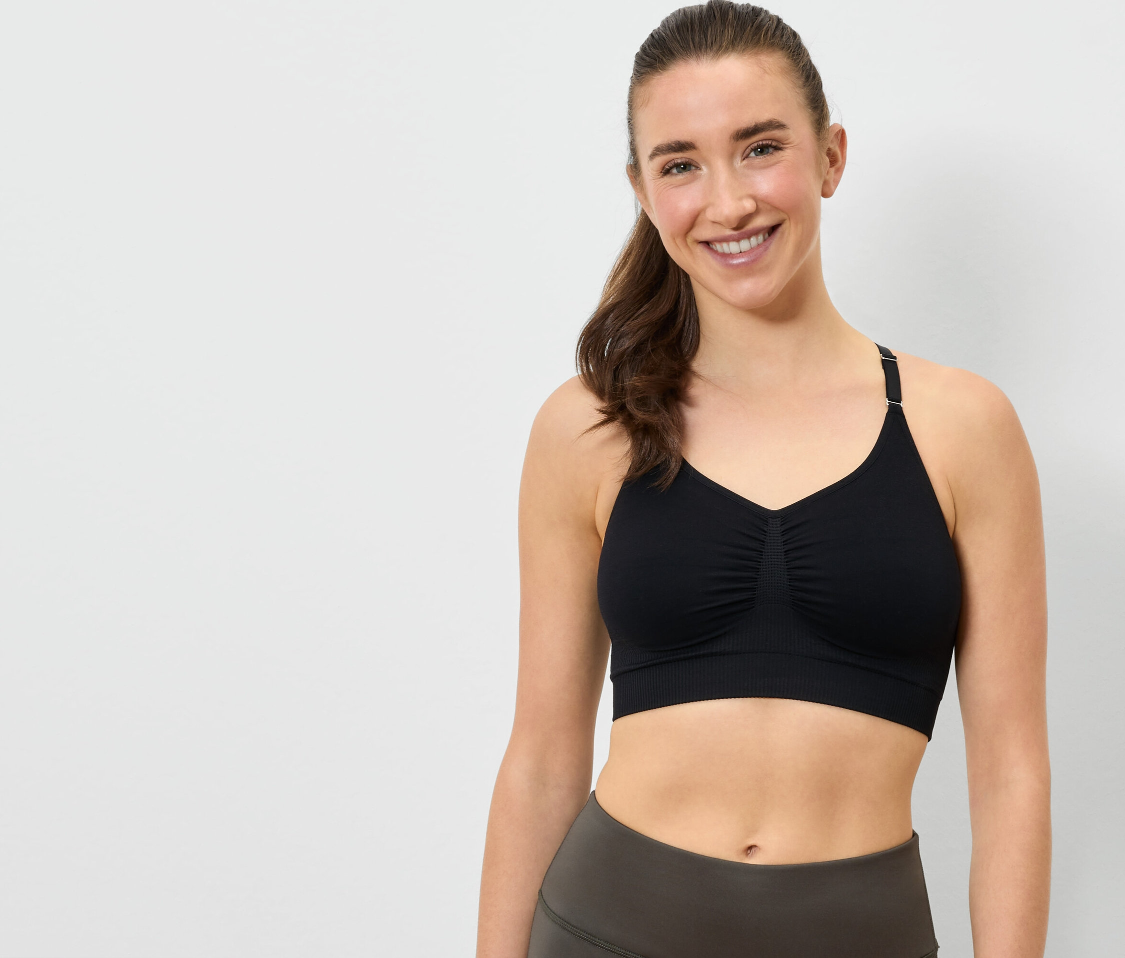Uśmiechnięta kobieta ma na sobie czarny biustonosz sportowy i szare legginsy.