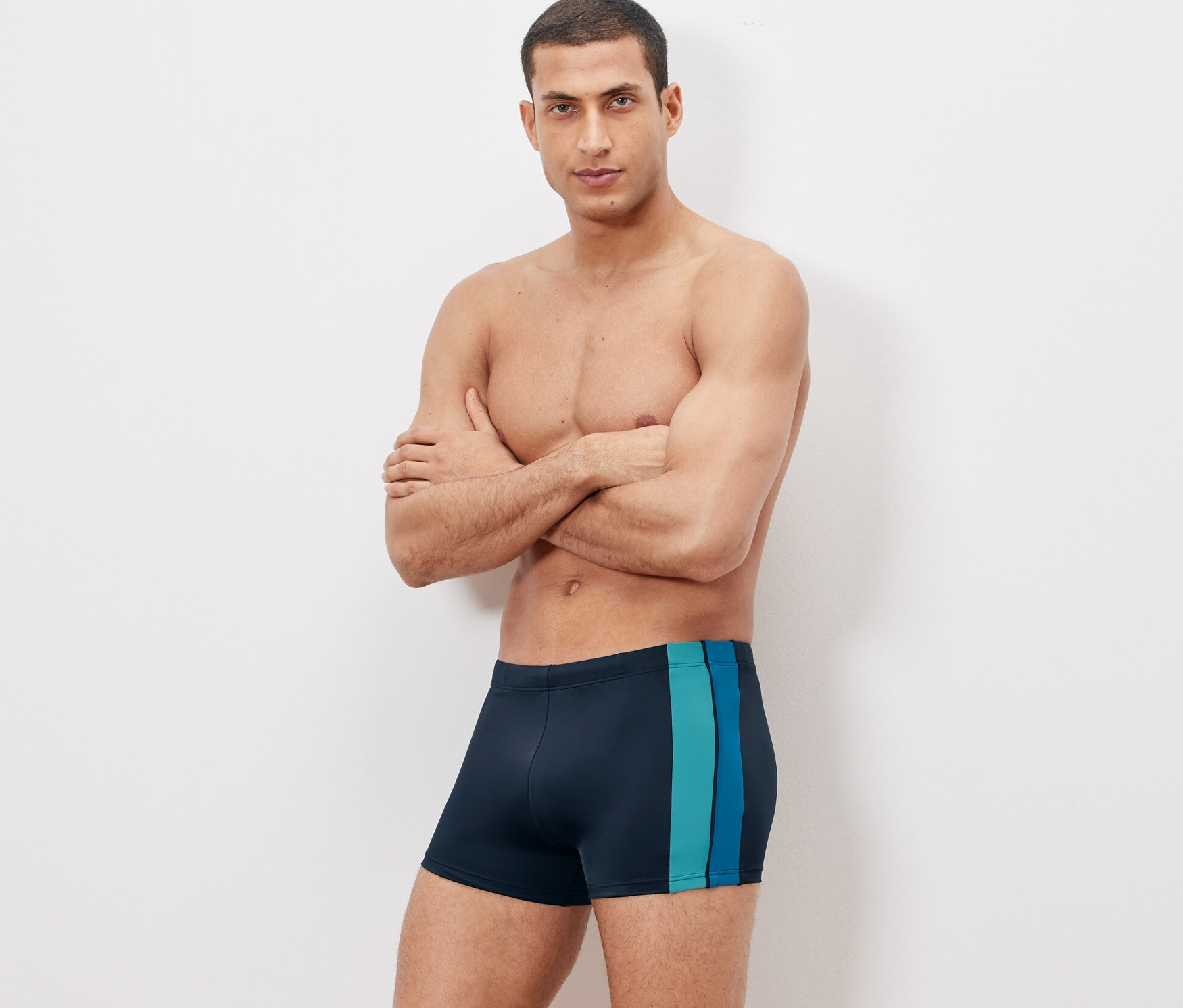 Mężczyzna pozuje ze skrzyżowanymi rękami w kąpielówkach.