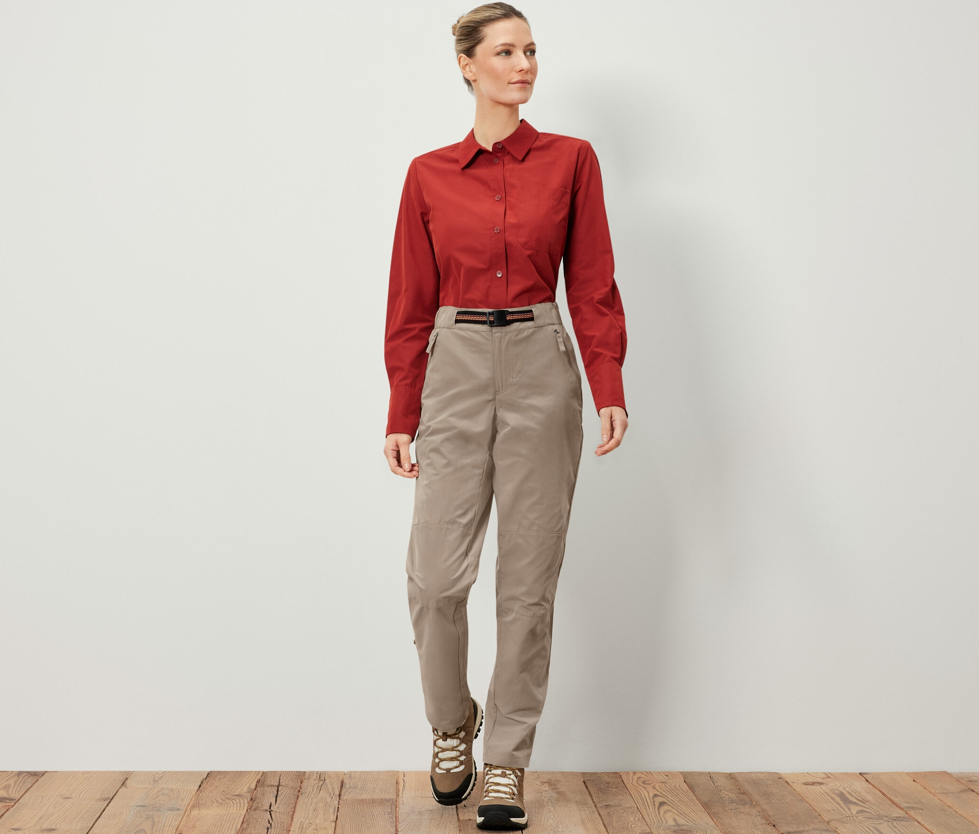 Kobieta ma na sobie spodnie outdoorowe z ochroną przed komarami, brązową koszulę i buty turystyczne.