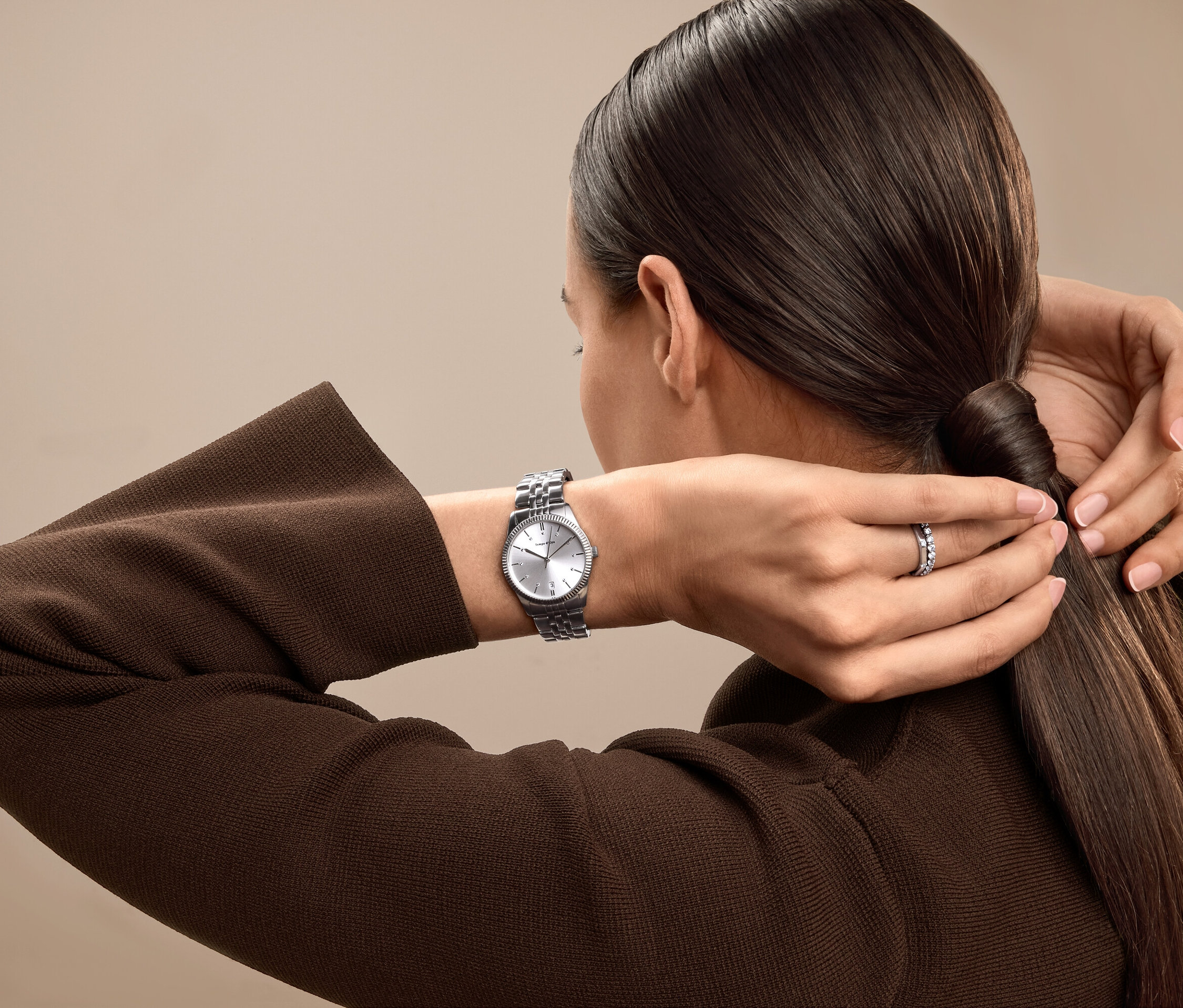 Kobieta związuje włosy w koński ogon, ma na sobie srebrny zegarek i pierścionek.