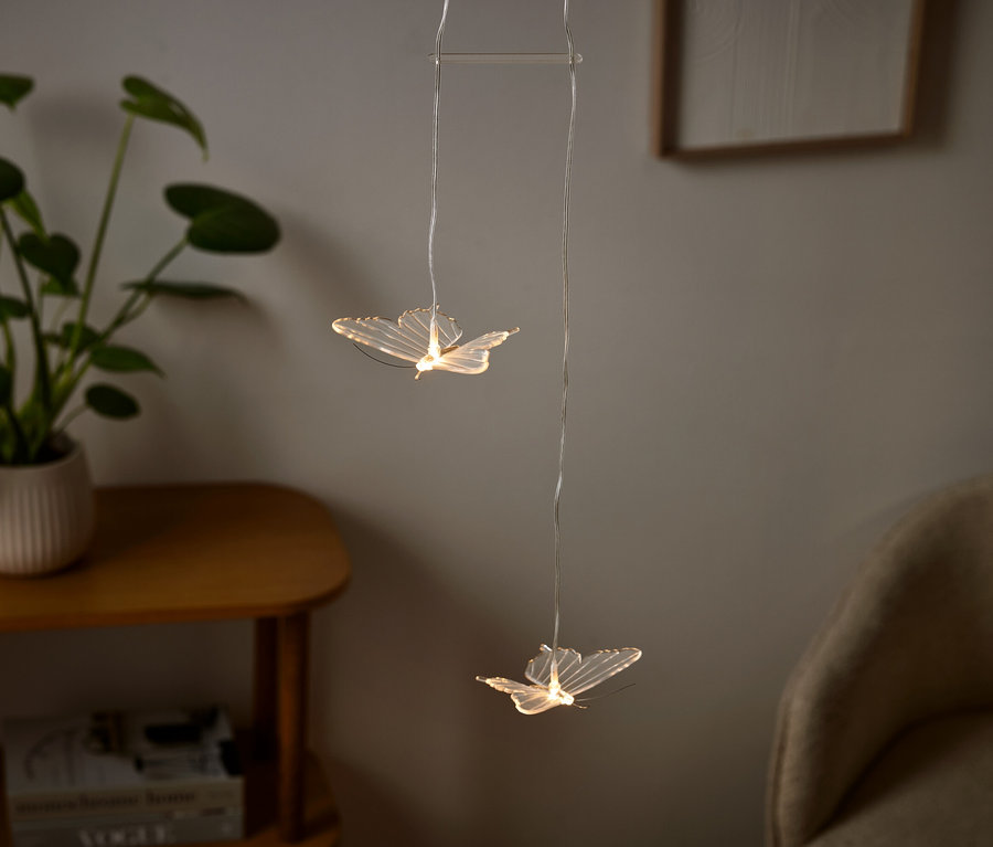 Dwa światła w kształcie motyli wiszą w pokoju, obok nich roślina w doniczce.
