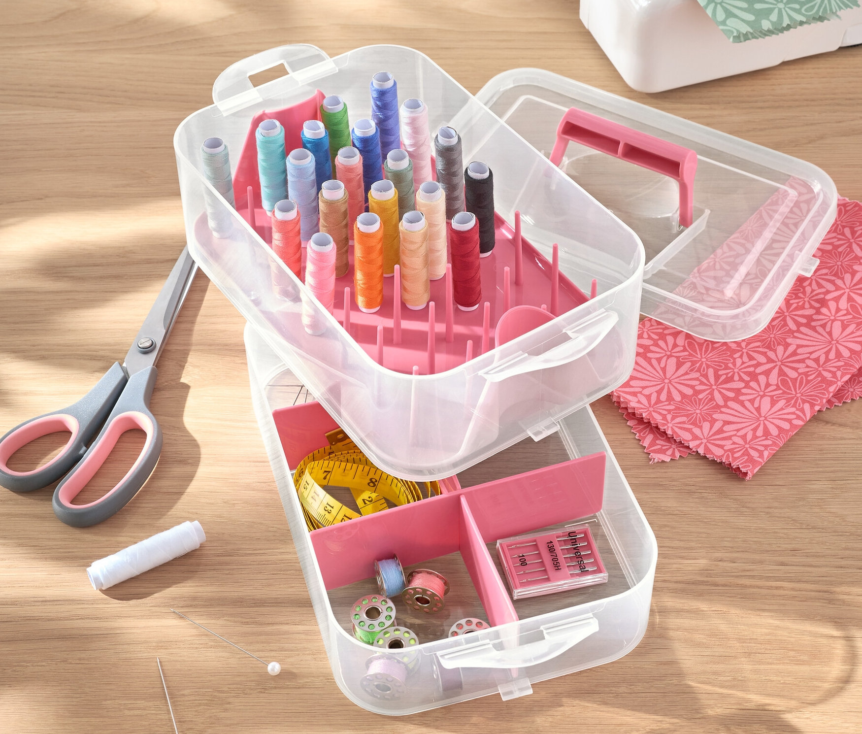 Otwarty plastikowy pojemnik na przybory z nićmi, nożyczkami, igłami i maszyną do szycia na stole.