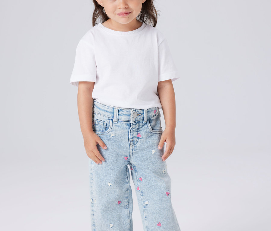 Dziewczynka w białej koszulce i jasnoniebieskich dżinsach we wzory serc i myszek.