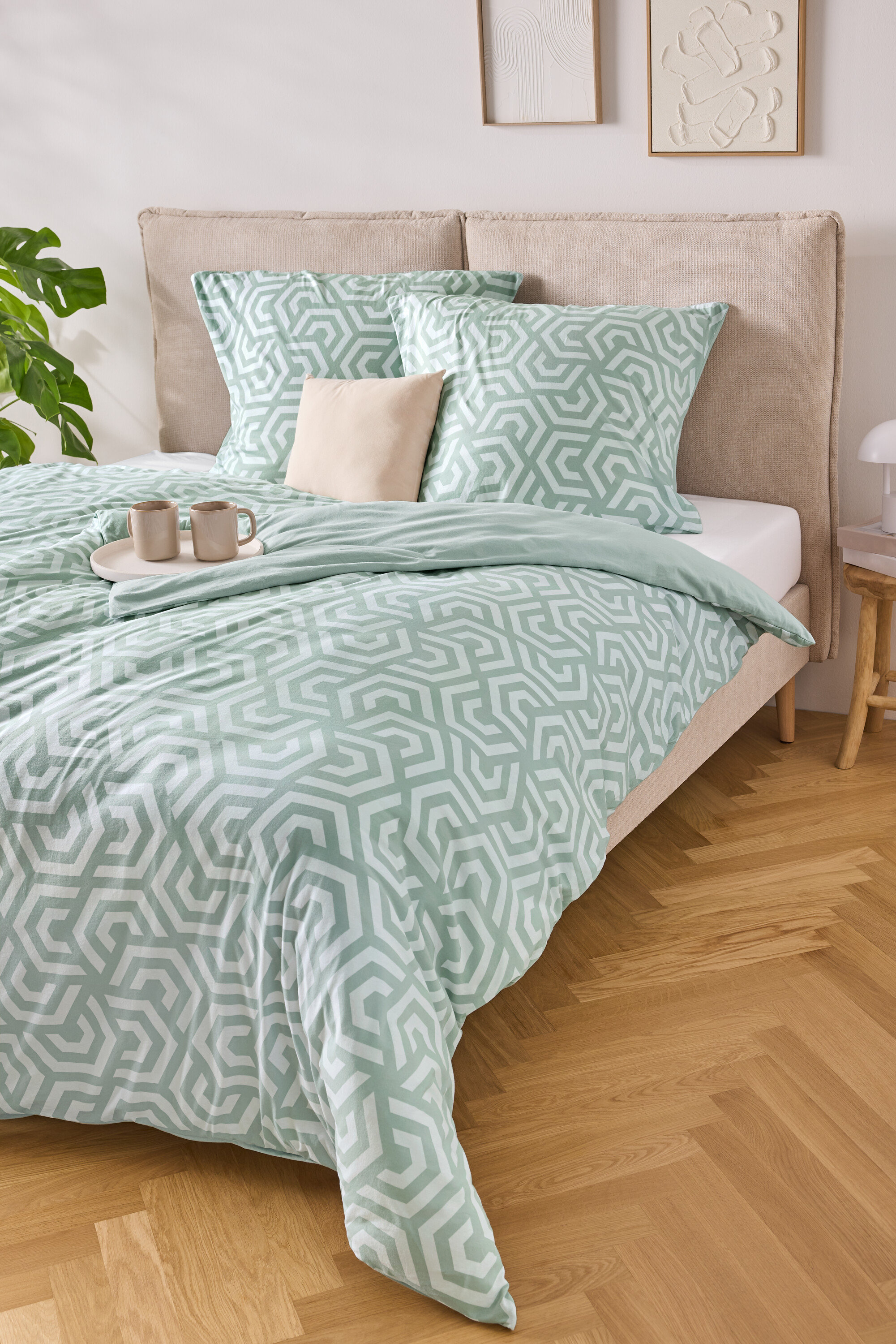 Łóżko z jasno-niebiesko-białą pościelą w paski, dwiema poduszkami i tacą z dwoma filiżankami.