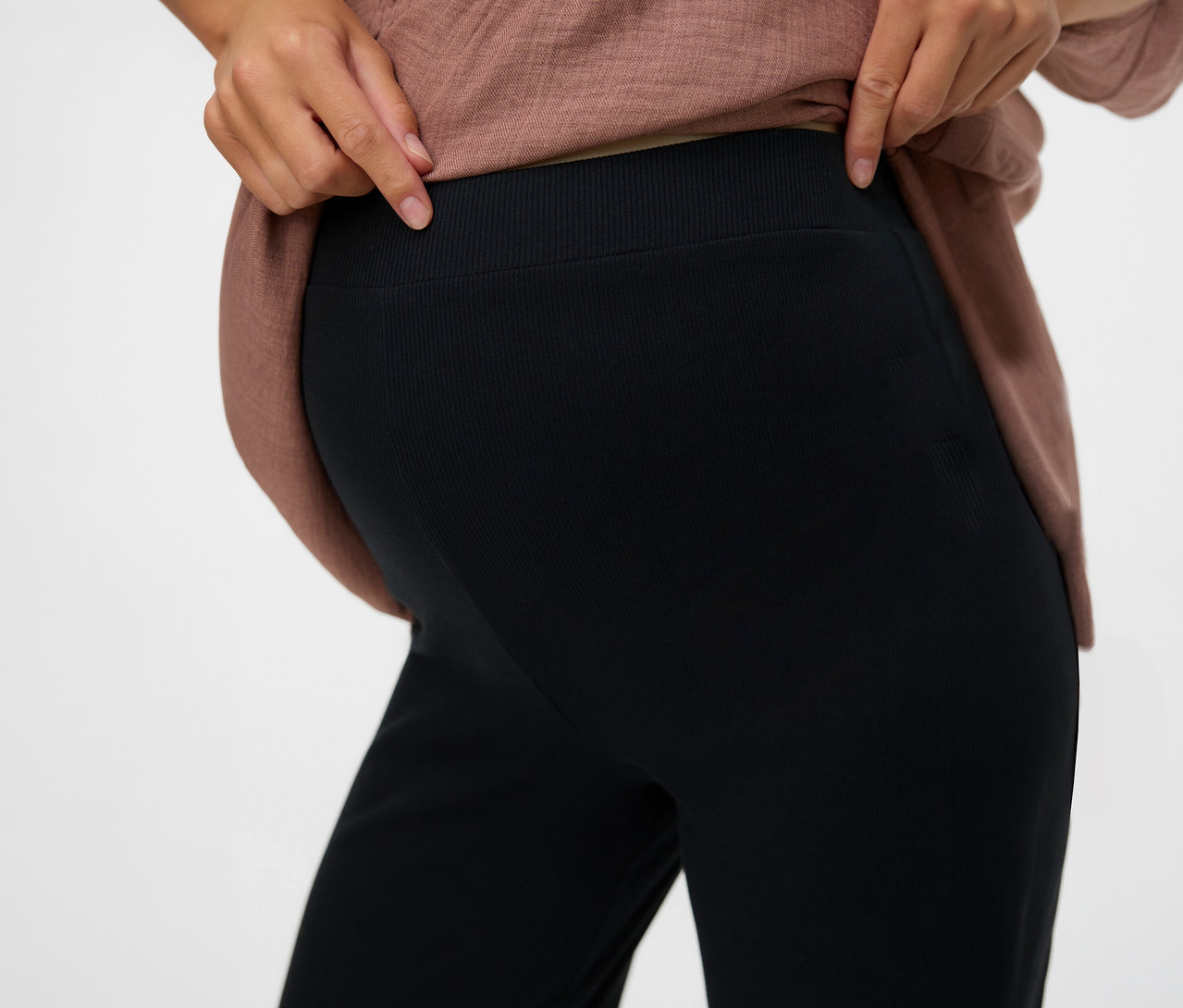 Kobieta pokazuje w pasie czarne, luźne legginsy „MLEMILY” firmy MAMALICIOUS.