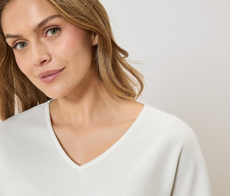 Portret kobiety o blond włosach w białym swetrze z dekoltem w serek.