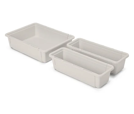 Trzy puste, beżowe plastikowe organizery do szuflad leżą na białym tle.