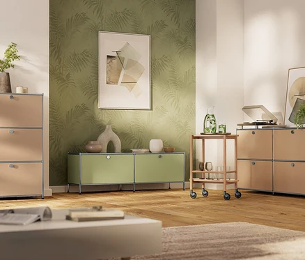 Nowoczesny salon z drewnianą podłogą i zieloną tapetą. Po lewej metalowa komoda „CN3” z 3 klapami w kolorze toffi. Na środku metalowa szafka typu lowboard „CN3” w kolorze pistacjowym. Po prawej metalowa szafka typu sideboard „CN3” z 4 klapami w kolorze toffi, na niej gramofon. Pomiędzy nimi drewniany wózek barowy z napojami.