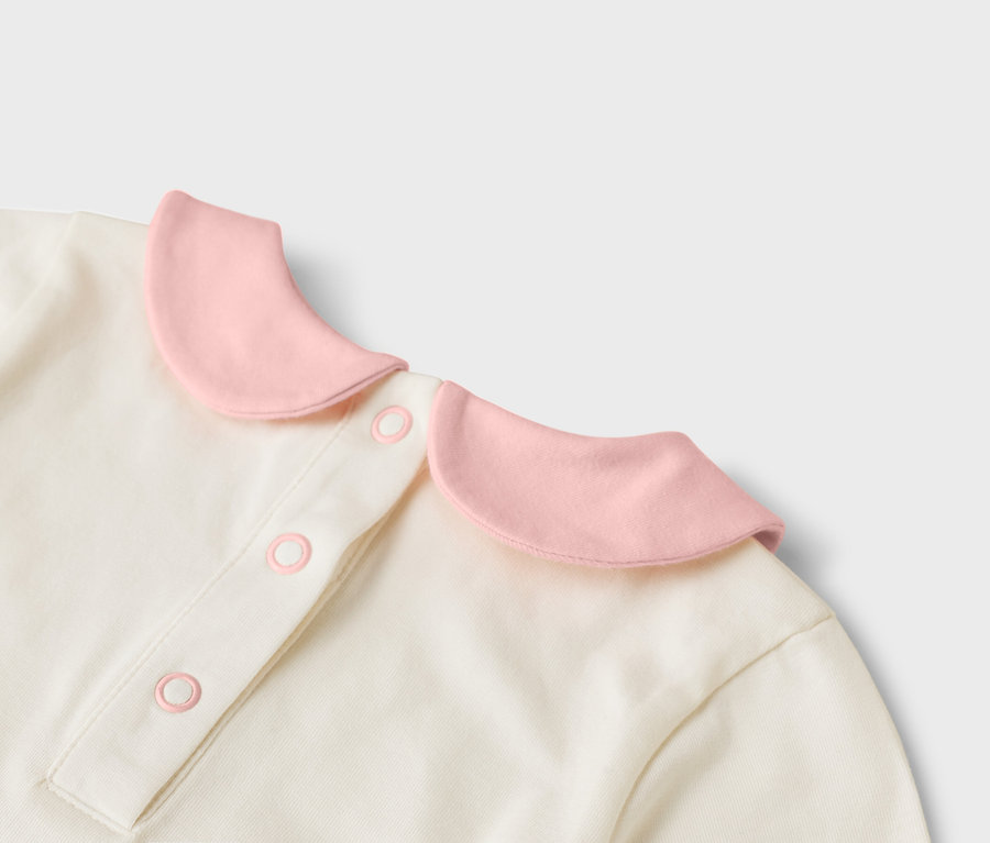 Szczegółowy widok kremowej bluzki z różowym kołnierzykiem i guzikami.