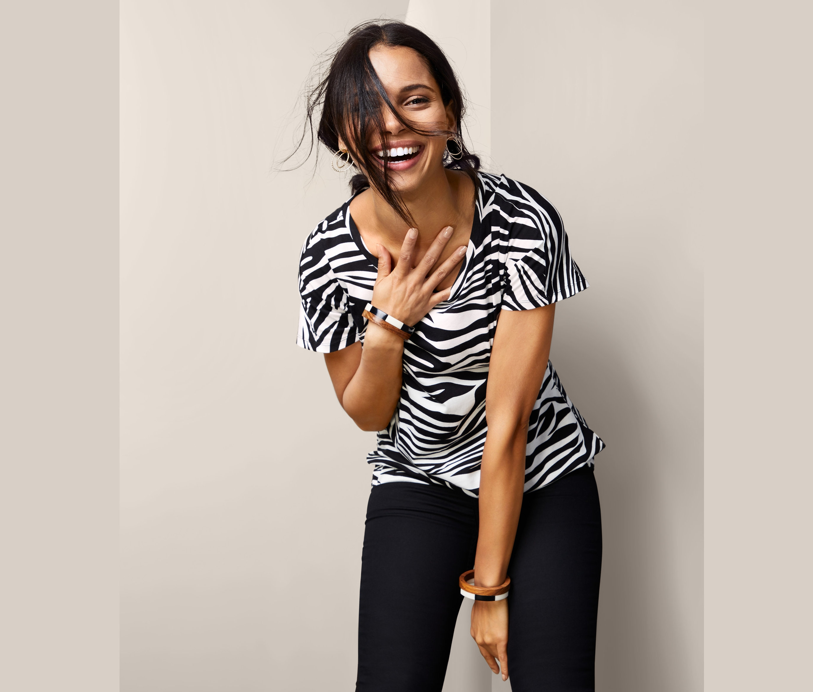 Uśmiechnięta kobieta z ręką na piersi ma na sobie bluzkę z krótkim rękawem w zwierzęcy wzór i czarne spodnie.
