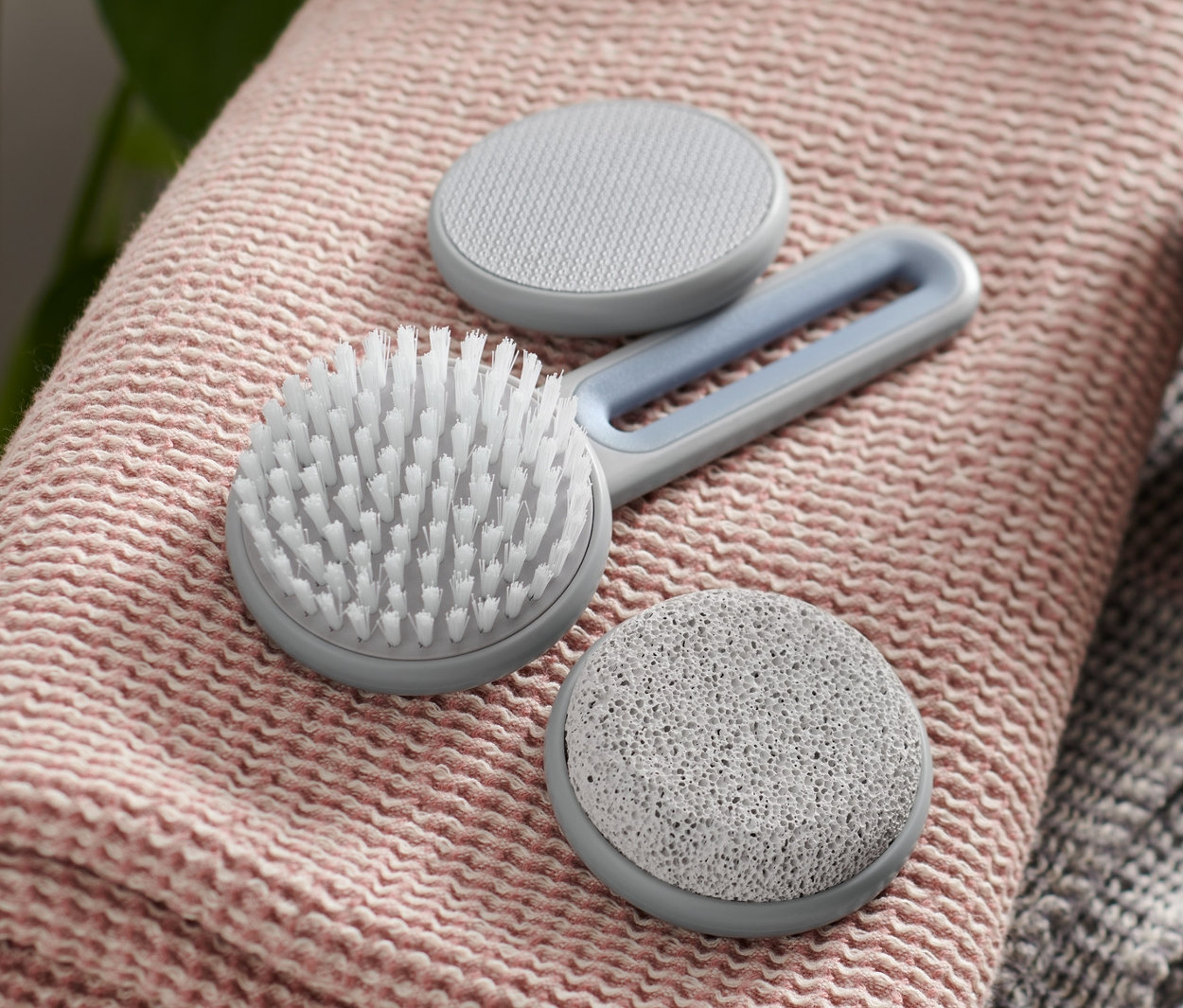 Zestaw do pielęgnacji stóp leży na różowym ręczniku obok brązowej butelki z dozownikiem.