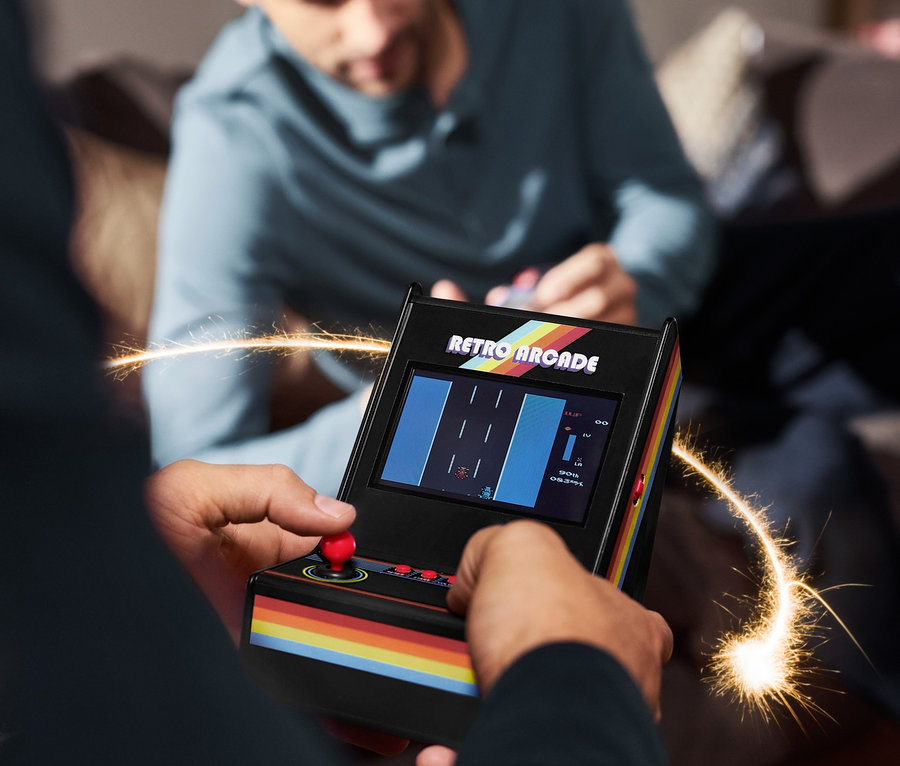 Mężczyzna gra na miniaturowym automacie do gry Arcade, w tle siedzi inny mężczyzna.