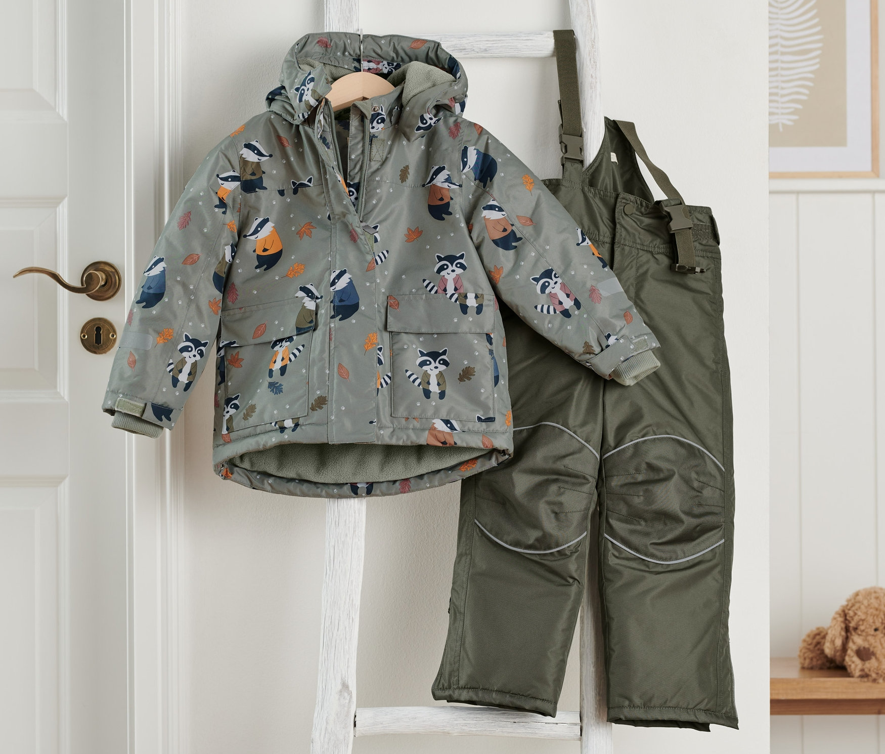 Dwuczęściowy kombinezon zimowy w kolorze oliwkowym zawieszony na drabinie.