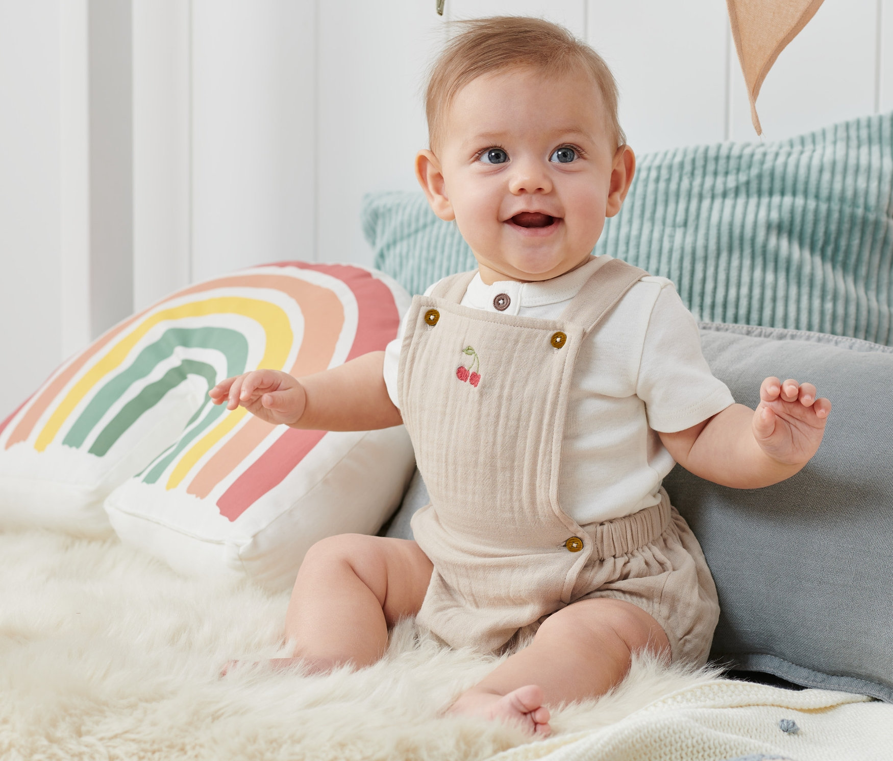 Uśmiechnięte dziecko siedzi na futrze i ma na sobie rampers niemowlęcy.