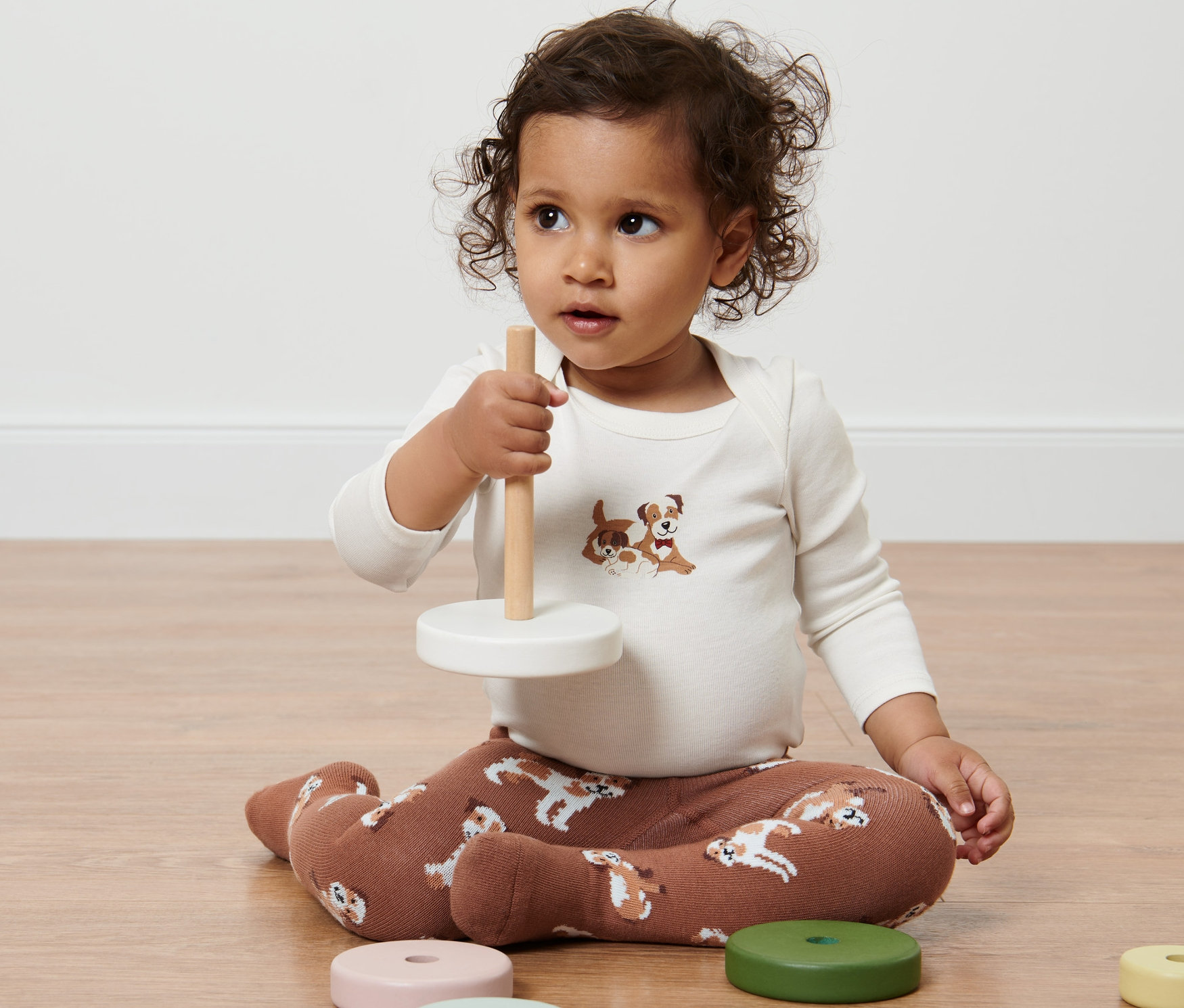 Dziecko siedzi na podłodze i bawi się zabawką. Ma na sobie Rajstopy, 2 pary z nadrukiem psów.