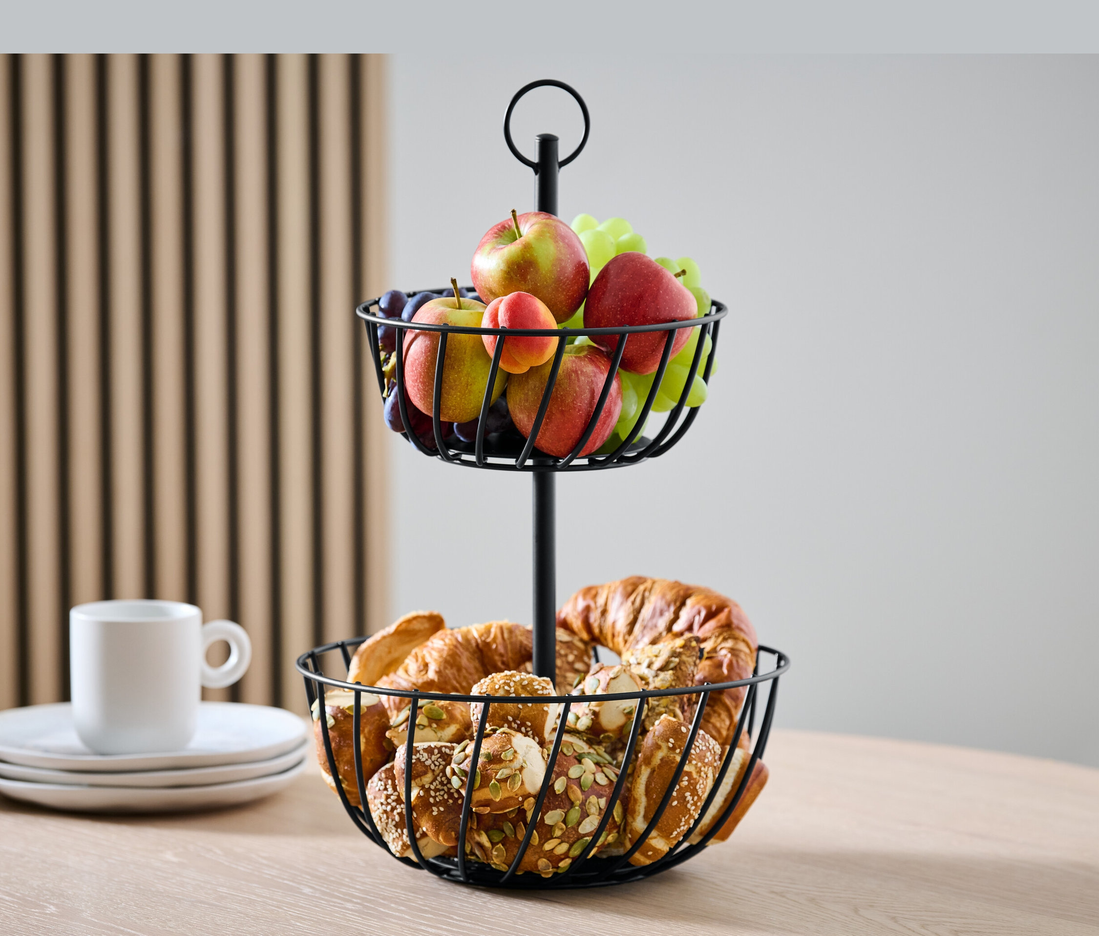 Dwu poziomowa etażerka z owocami i pieczywem na stole.