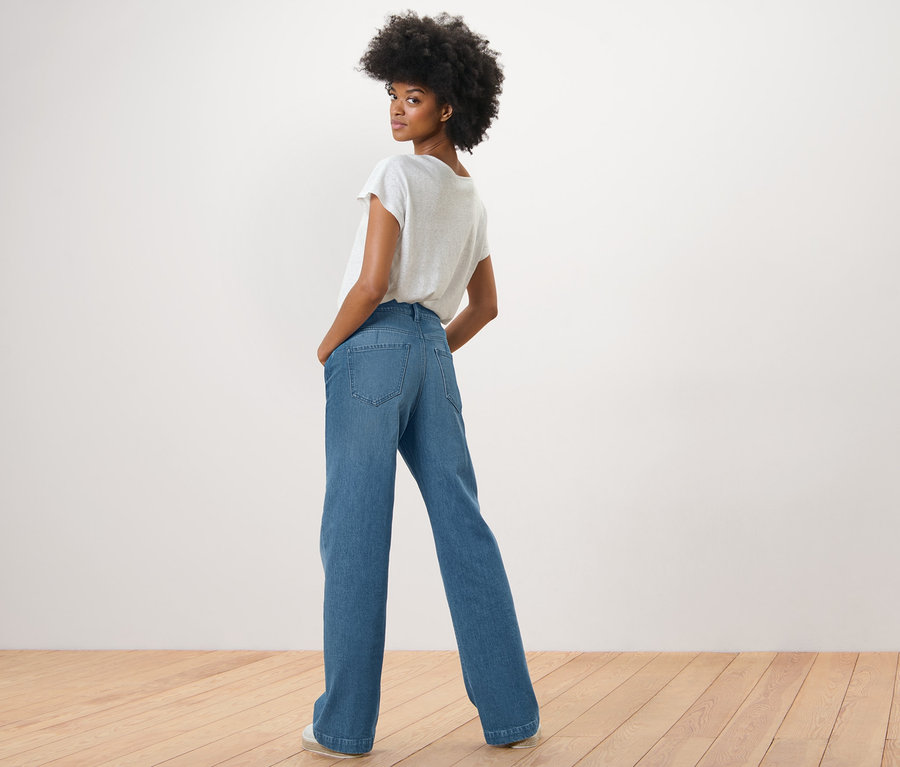 Kobieta spogląda przez ramię i pozuje w dżinsach palazzo – fason „Neni” i białym T-shircie.