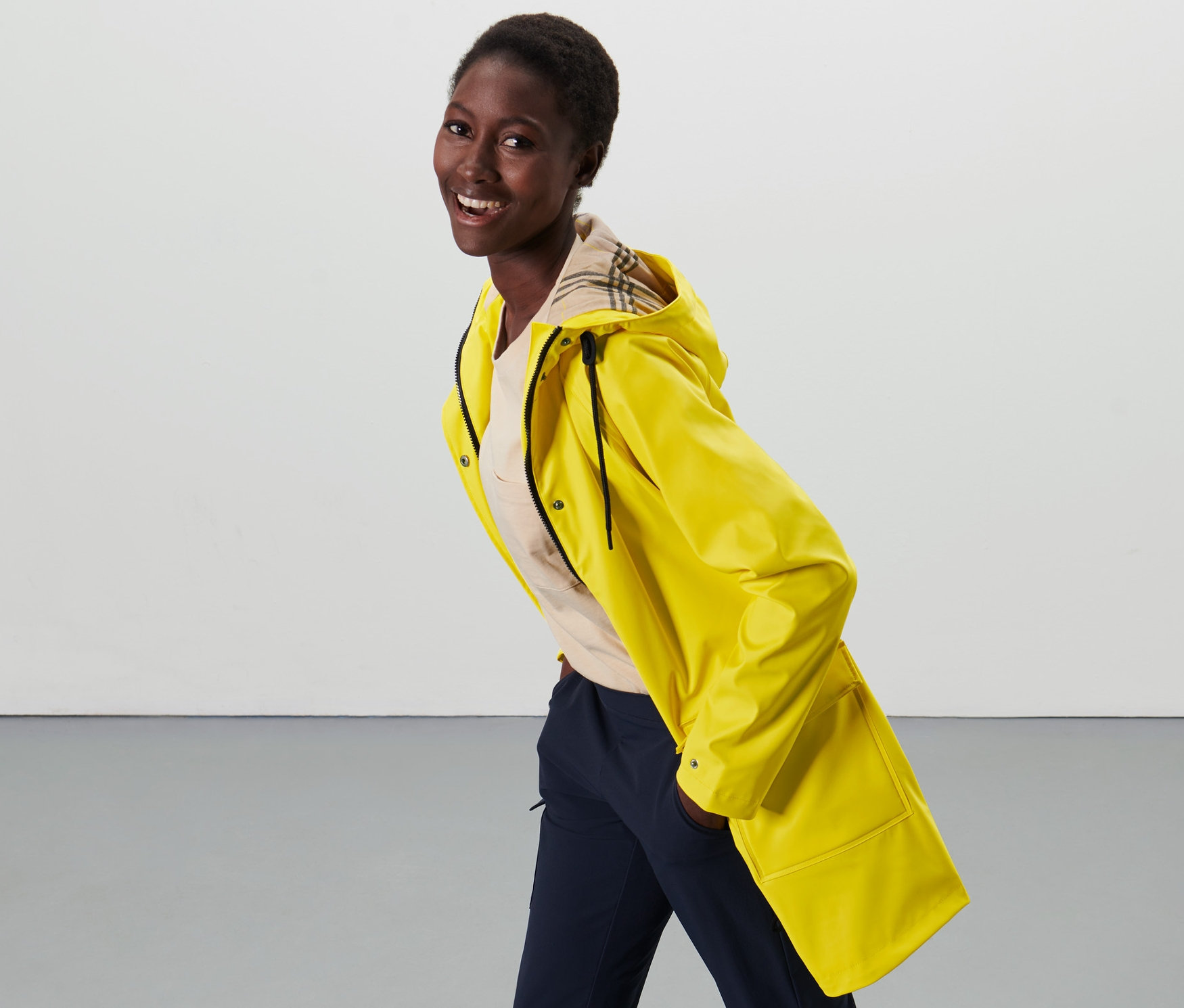 Kobieta pozuje w żółtej parce przeciwdeszczowej w stylu rybackim i granatowych spodniach.