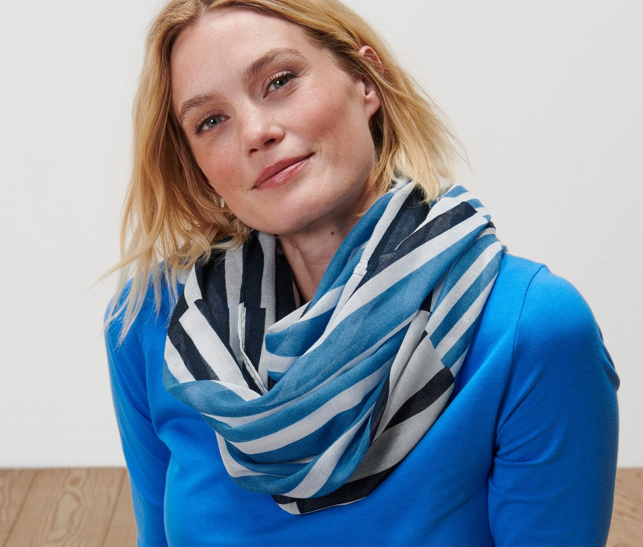 Blondynka siedzi na podłodze i ma na sobie szal-komin w paski.