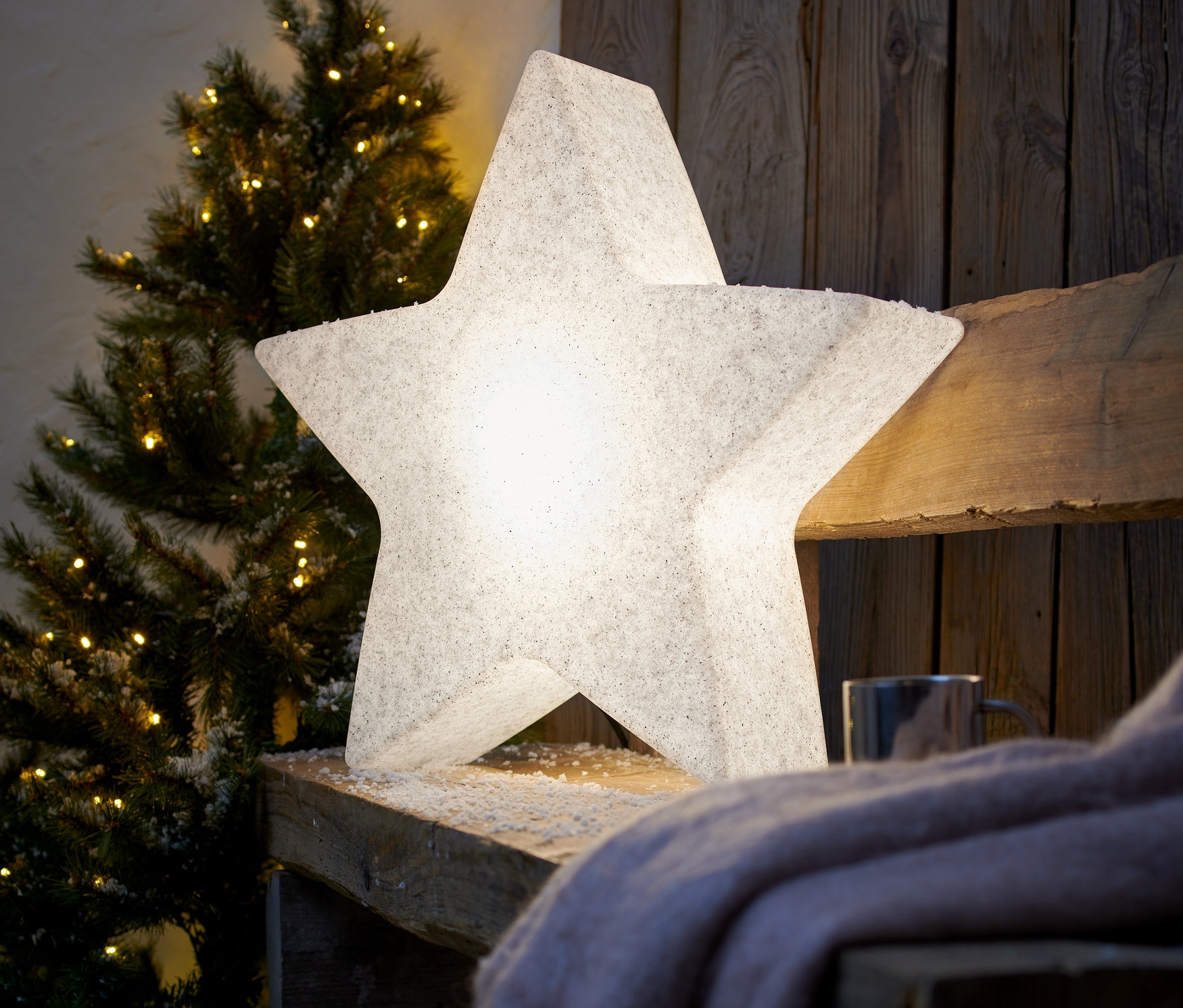 Dwie inteligentne lampy ogrodowe »Gwiazda«, S, na drewnianej ławce obok choinki.