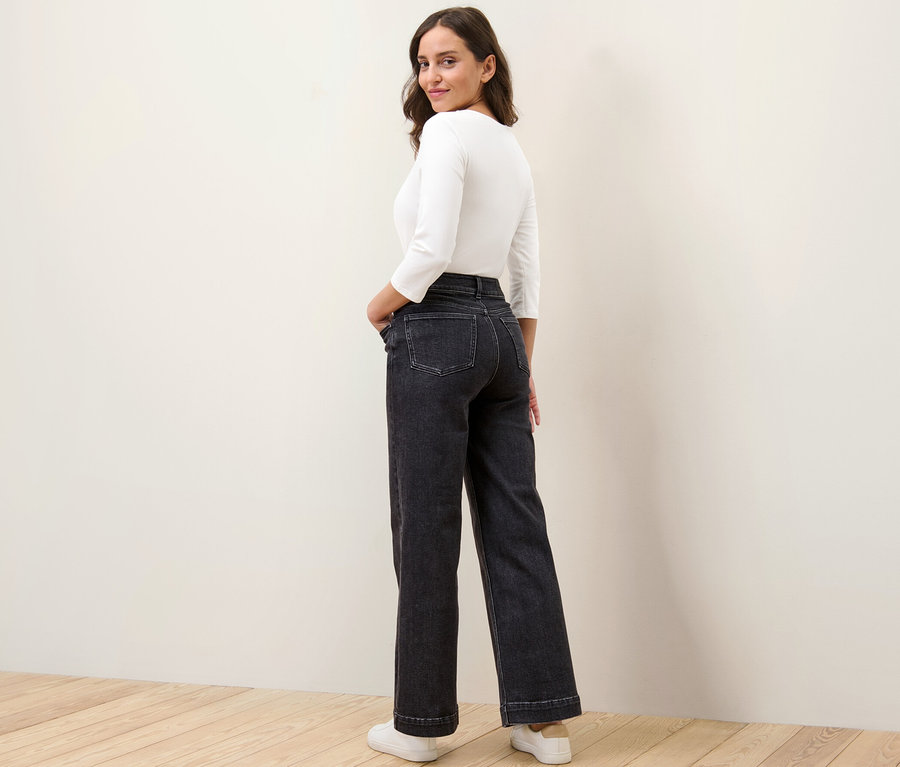 Kobieta spogląda przez ramię i pozuje w szerokich spodniach dżinsowych – fason „Viki”.