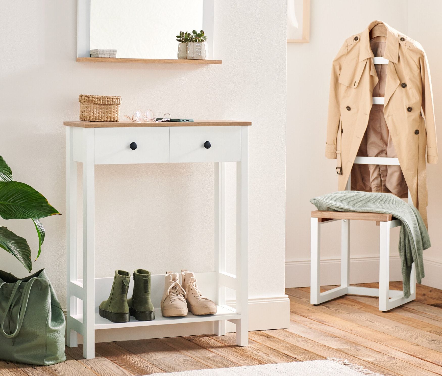 Przedpokój z konsolą z dwiema szufladami i stojącym wieszakiem na ubrania. Na konsoli leżą klucze i wiklinowy koszyk. Pod konsolą stoją buty, obok zielona torba.
