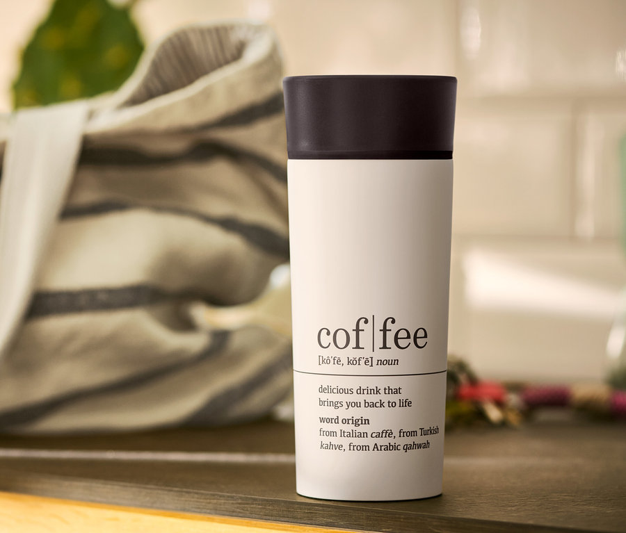 Biały kubek termiczny na kawę Coffee Dictionary z czarnym wieczkiem na stole.