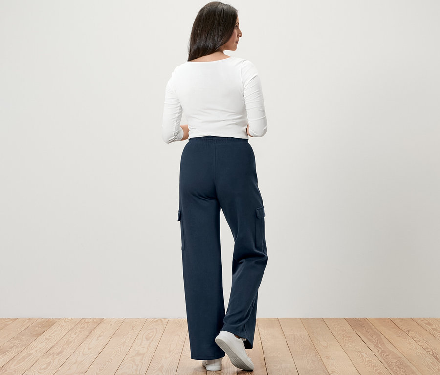 Kobieta stoi tyłem do aparatu, ubrana w granatowe spodnie dresowe z kieszeniami typu cargo.