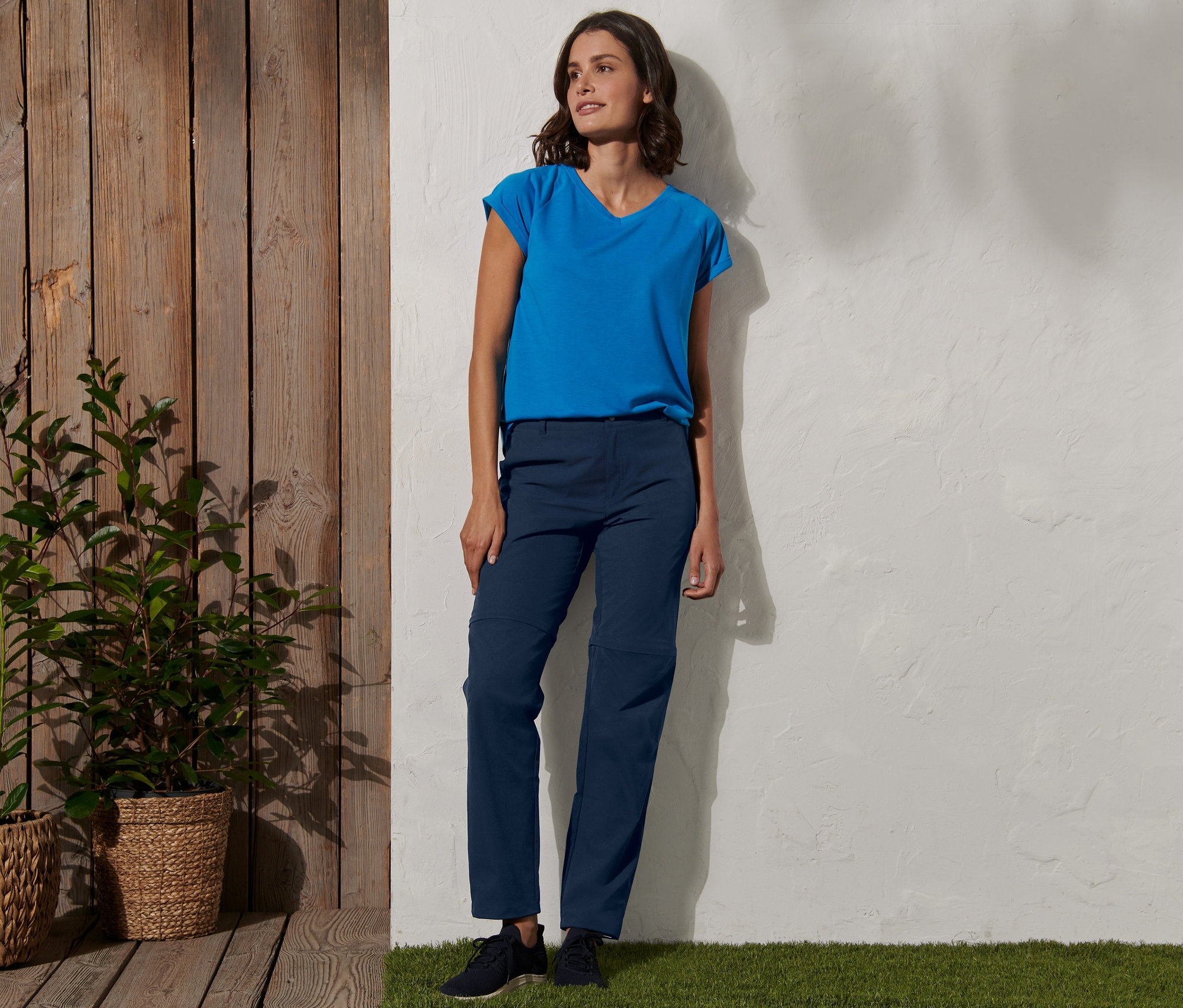 Kobieta stoi oparta o ścianę, ubrana w niebieskie spodnie funkcyjne 2 w 1.