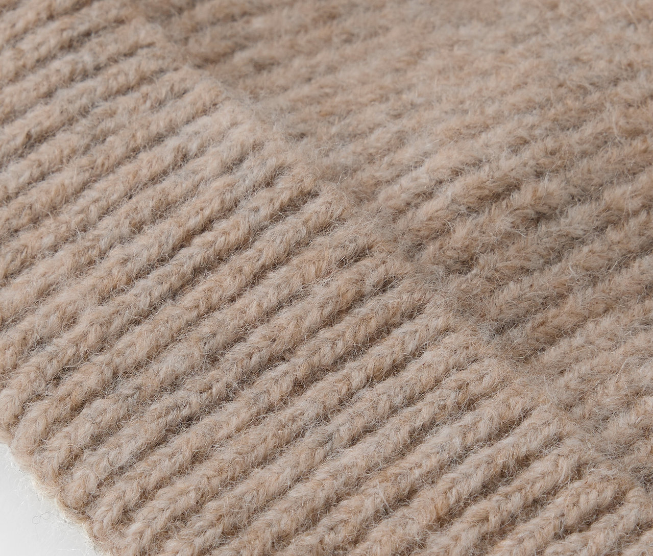 Zbliżenie na teksturę dzianiny beżowej czapki.