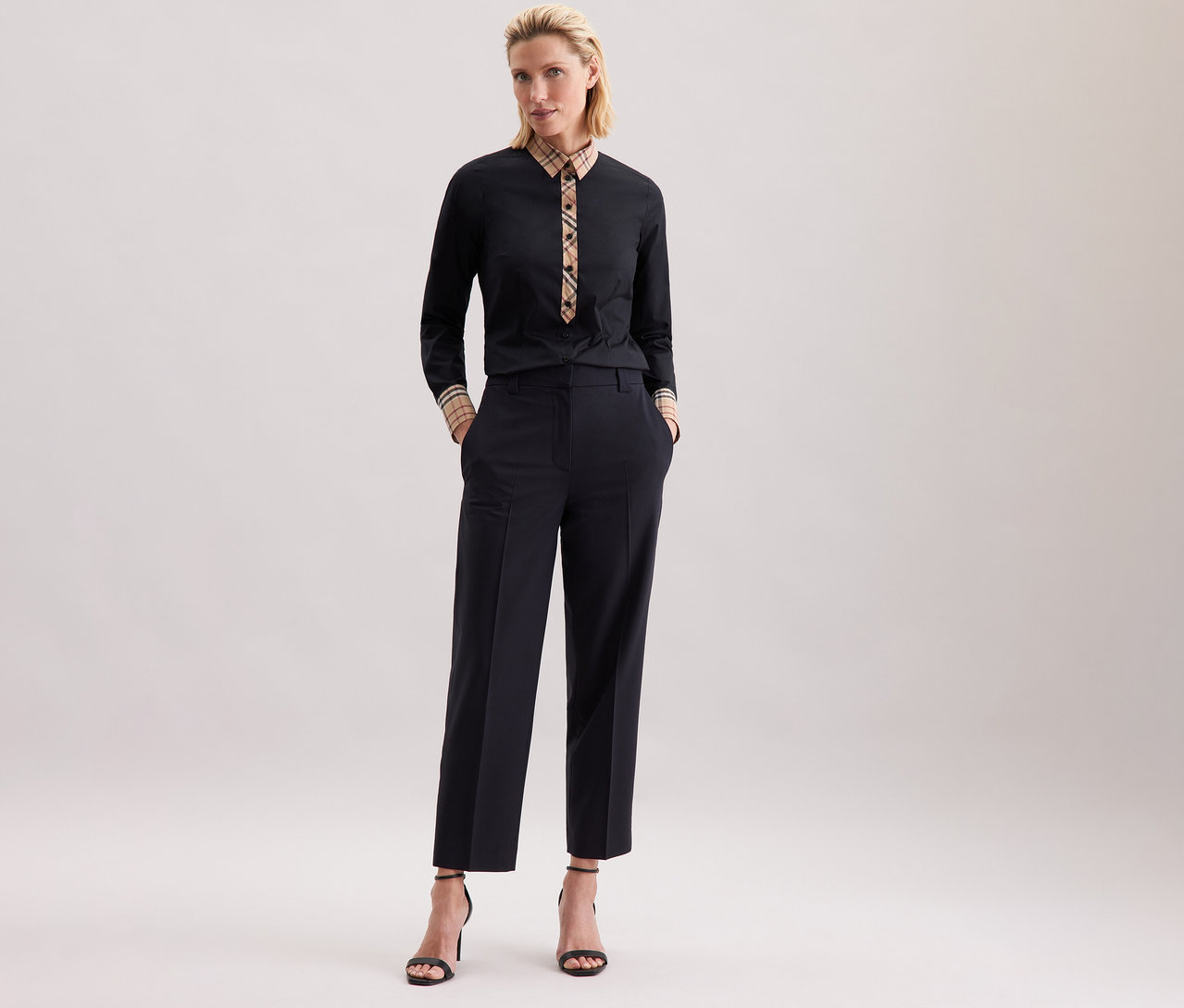 Kobieta pozuje w czarnej popelinowej bluzce Seidensticker z kratą i ciemnych spodniach.