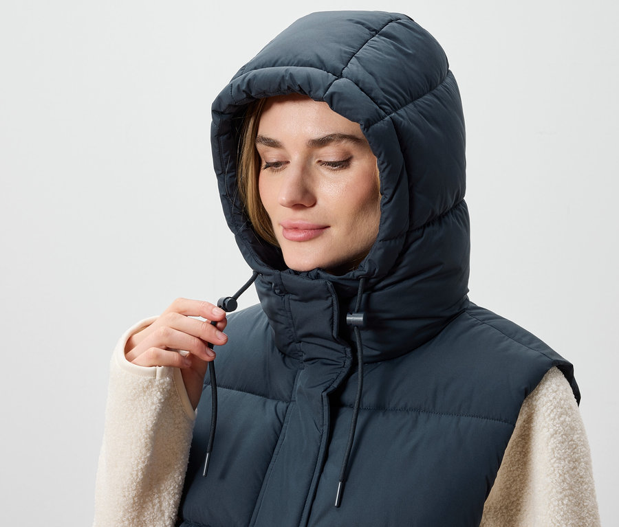 Kobieta reguluje kaptur granatowej, pikowanej kamizelki.