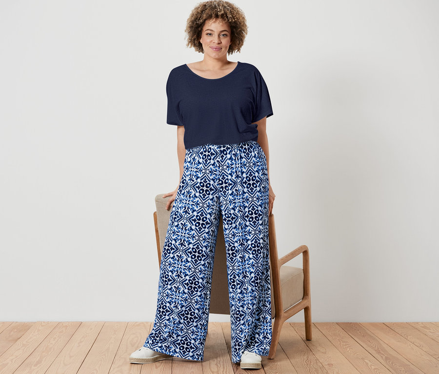 Kobieta pozuje w granatowej bluzce z zawartością lnu i granatowych, wzorzystych spodniach palazzo.