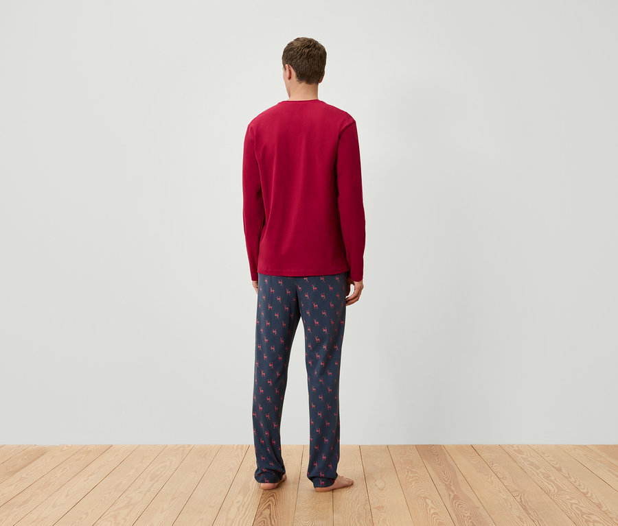 Mężczyzna tyłem do kamery ma na sobie czerwoną koszulkę piżamową z długim rękawem i granatowe spodnie piżamowe we wzór reniferów.