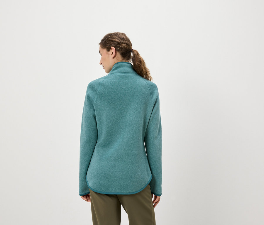 Kobieta tyłem do aparatu ma na sobie turkusowo-zieloną bluzę polarową i oliwkowo zielone spodnie.