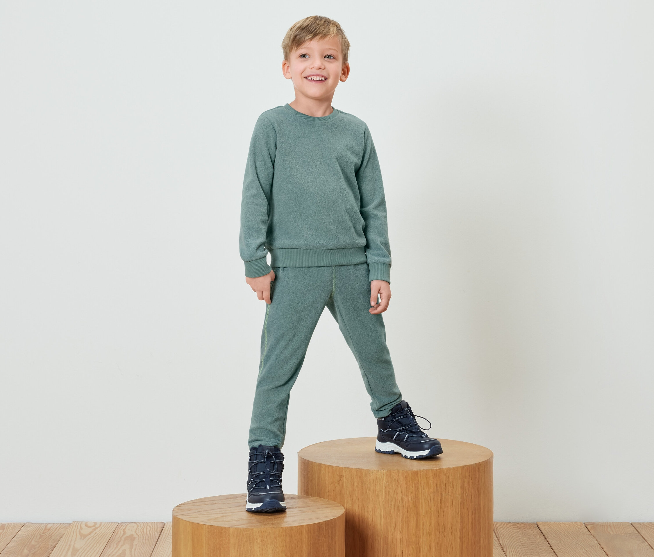 Chłopiec w zielonym dresie stoi na drewnianym cokole.