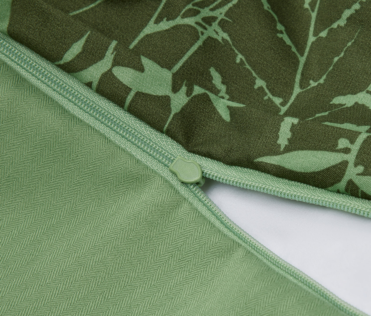 Zbliżenie na zieloną poszewkę na poduszkę z kwiatowym wzorem i zamkiem błyskawicznym.