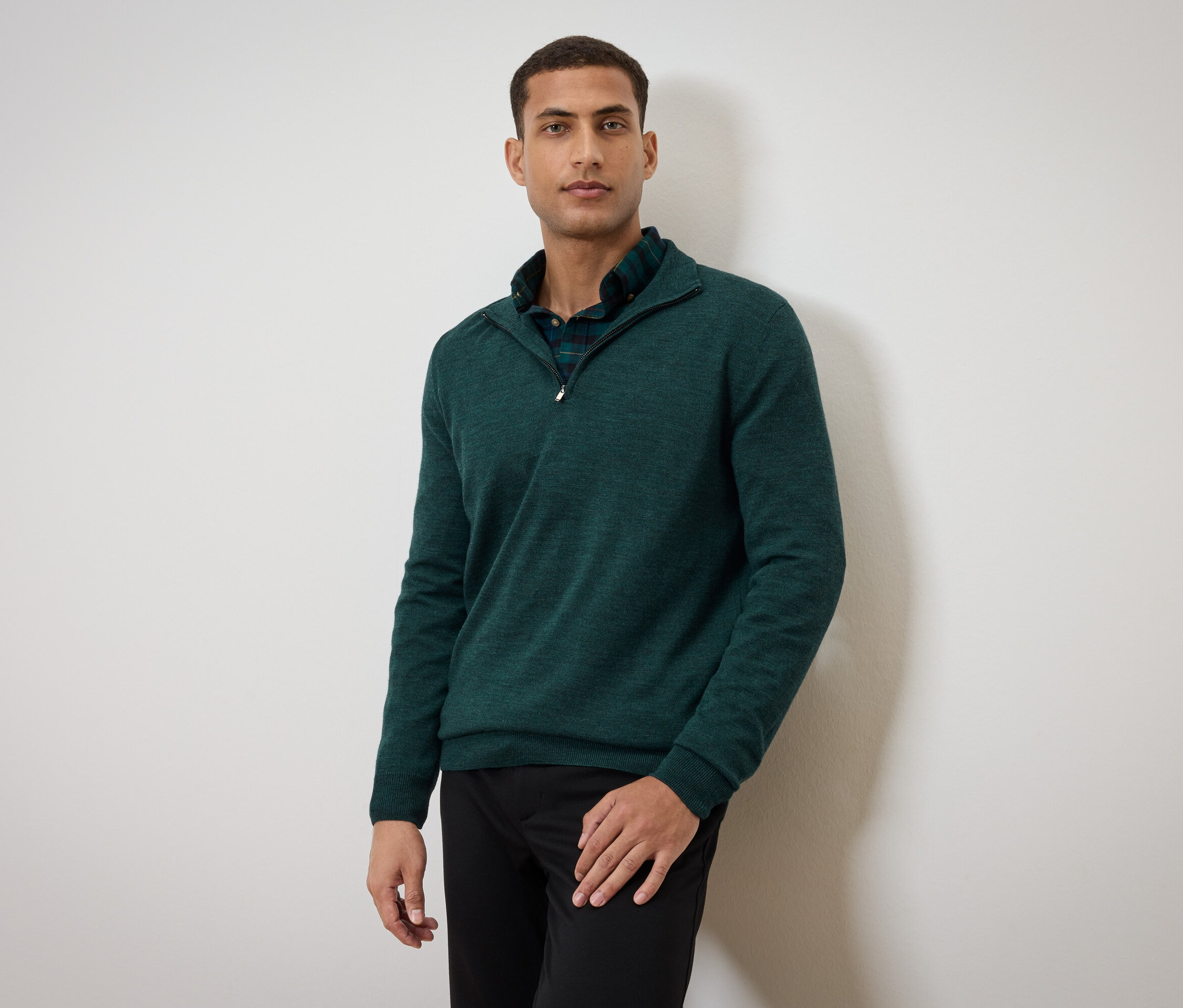 Mężczyzna pozuje w zielonym swetrze i czarnych spodniach.
